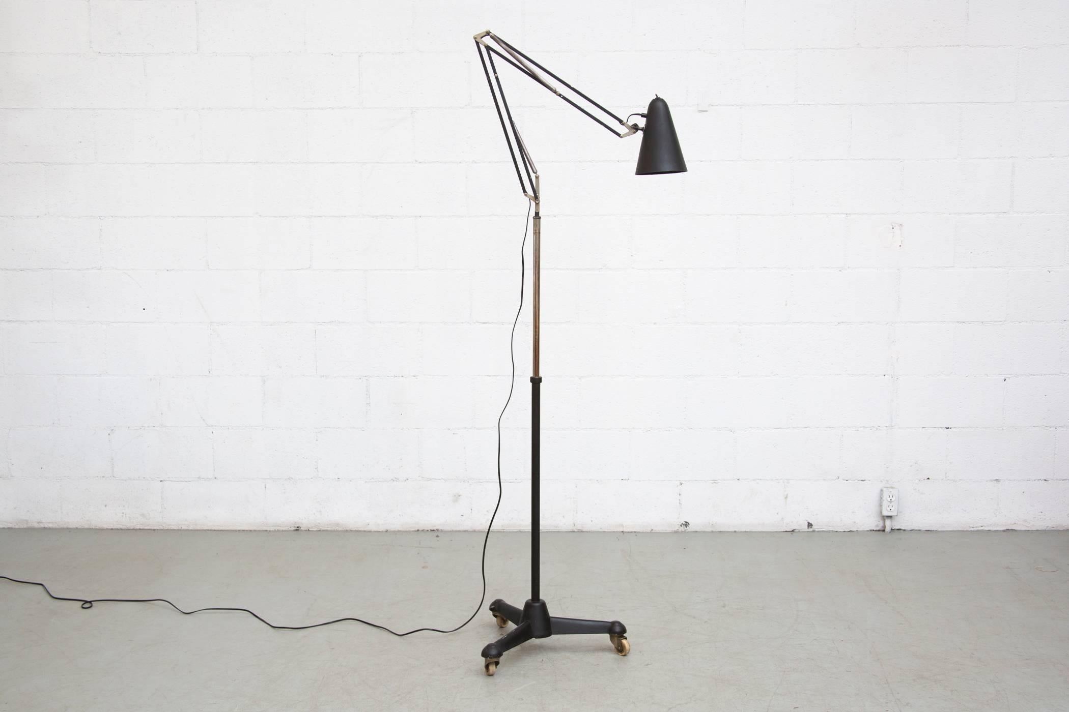 An original black enameled rolling drafting floor lamp with tripod base. In original condition with slight wear consistent with age and use.