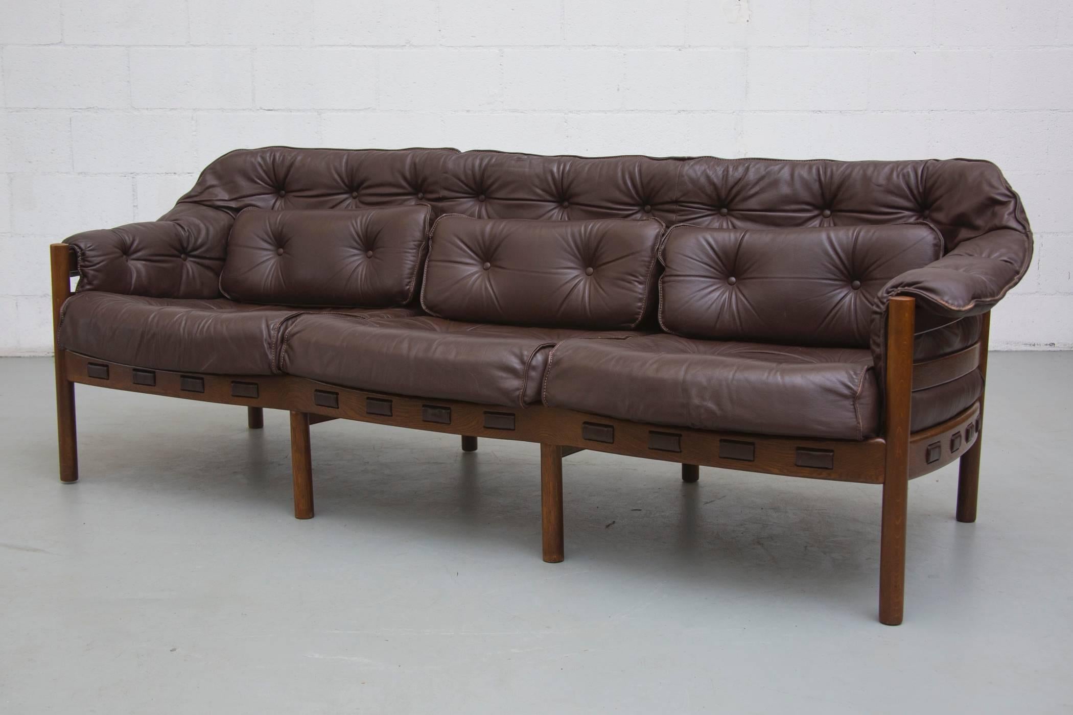 Lovely three-seat wood framed sofa with tufted leather back, seat cushions and pillows in original condition with visible signs of wear consistent with its age and usage.