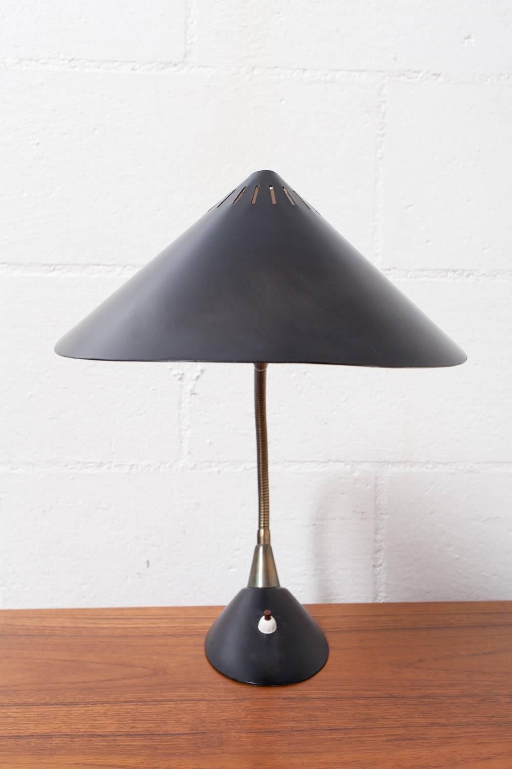 Black enameled metal leaf-shaped shade with line cut-outs. Adjustable brass goose neck with bakelite button on black enameled base. Some rusting/ discoloration inside shade due to age and wear.