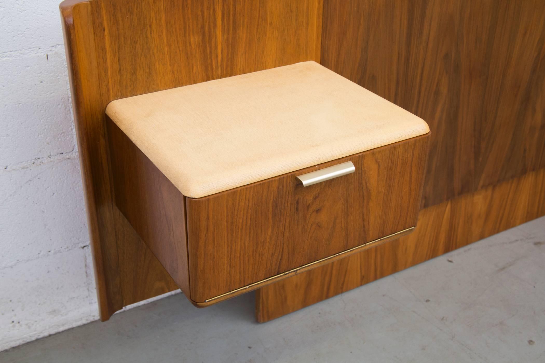 Walnut headboard with floating night stands topped with vanilla textured material and brass toned pulls. One night stand has a drop down door; the other has two stacking drawers. Both with birch interior. Headboard in good original condition with