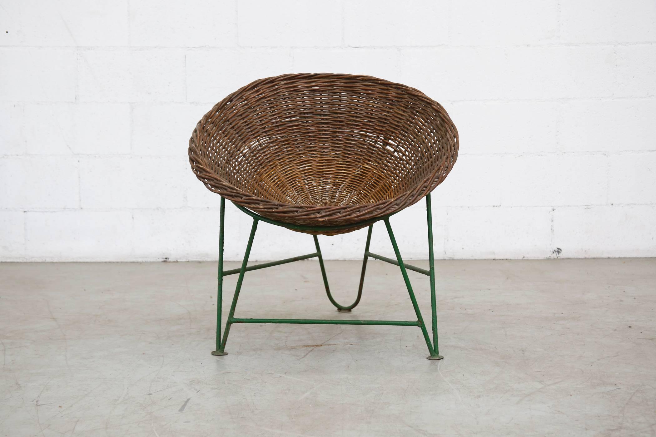 Beautiful woven bucket seat with visible fading and patina that sits in a green enameled metal base, also with visible wear and patina.
 