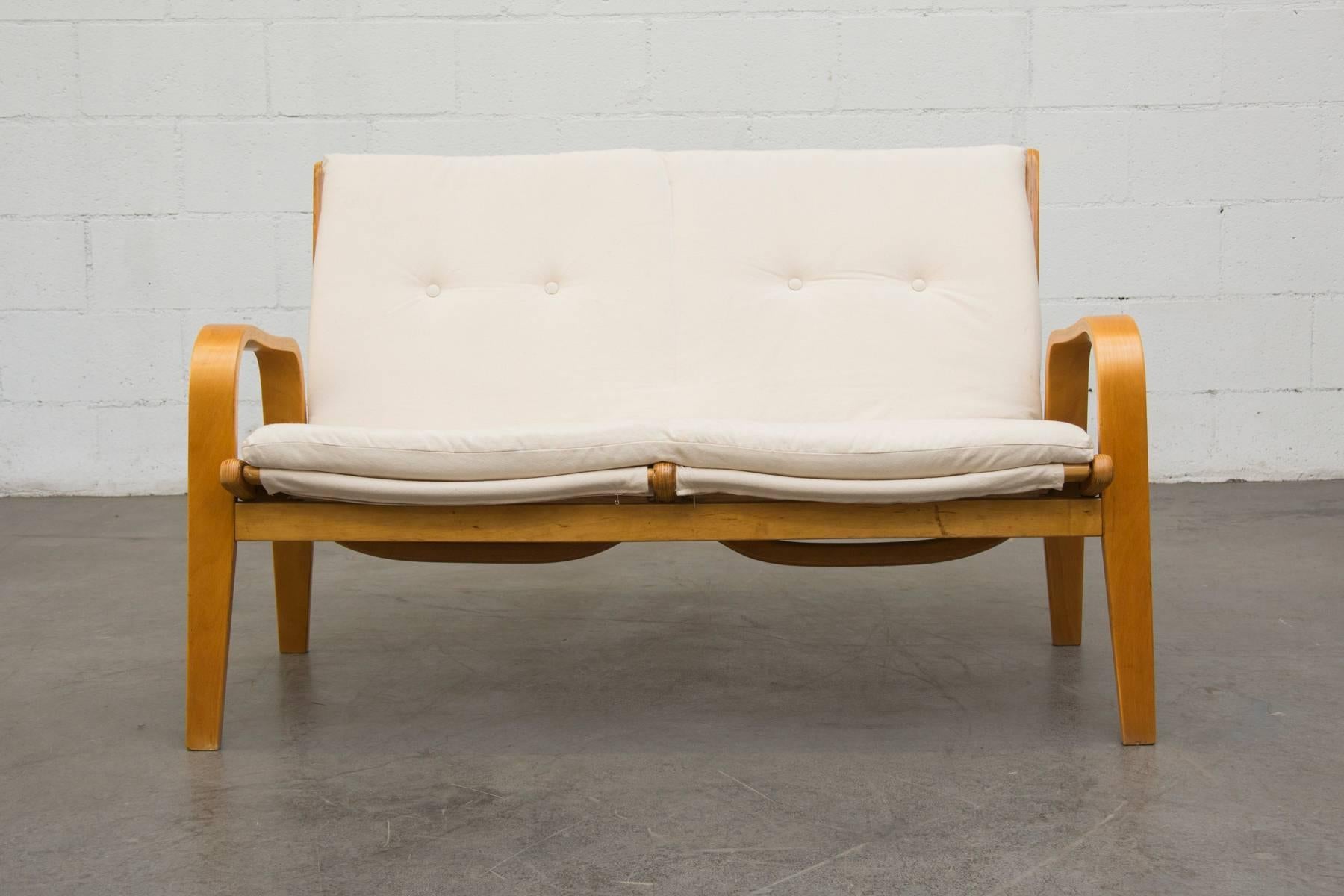Alvar Aalto style bent birch framed loveseat with original strapping and new natural canvas cushion. Pastoe easy chair (model FB06) designed by Cees Braakman for UMS Pastoe in the 1950s. Loveseat may vary slightly from the one photographed as there
