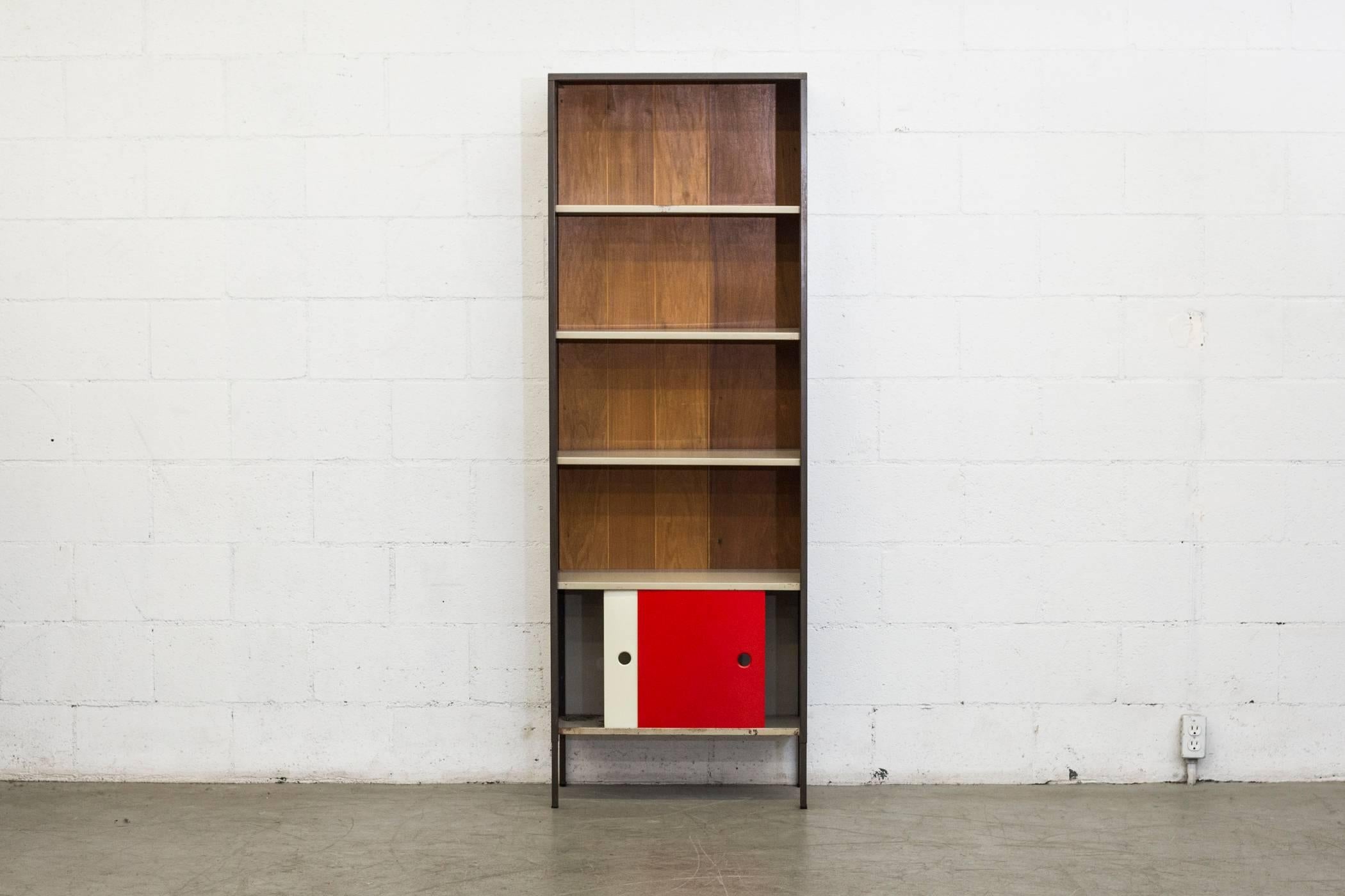 Dark grey enameled metal cabinet with wood paneled backing, grey enameled metal shelves over a small cabinet with red and bone white enameled metal sliding doors. In original condition with some wear to enamel. Also available and shown with ST119 BW