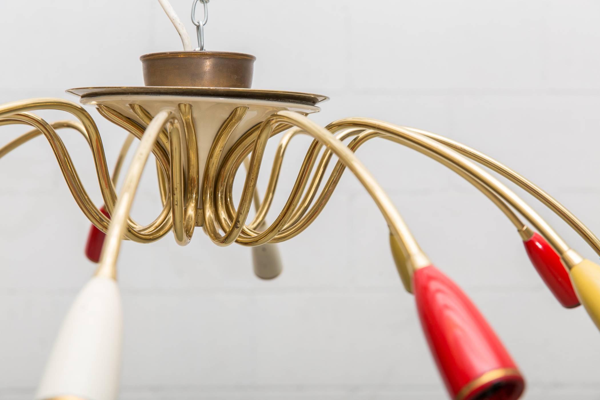 Delicate twelve-armed enameled metal and brass flush mount chandelier. Pimento, mustard and cream colored socket casings. Original condition with visible age.