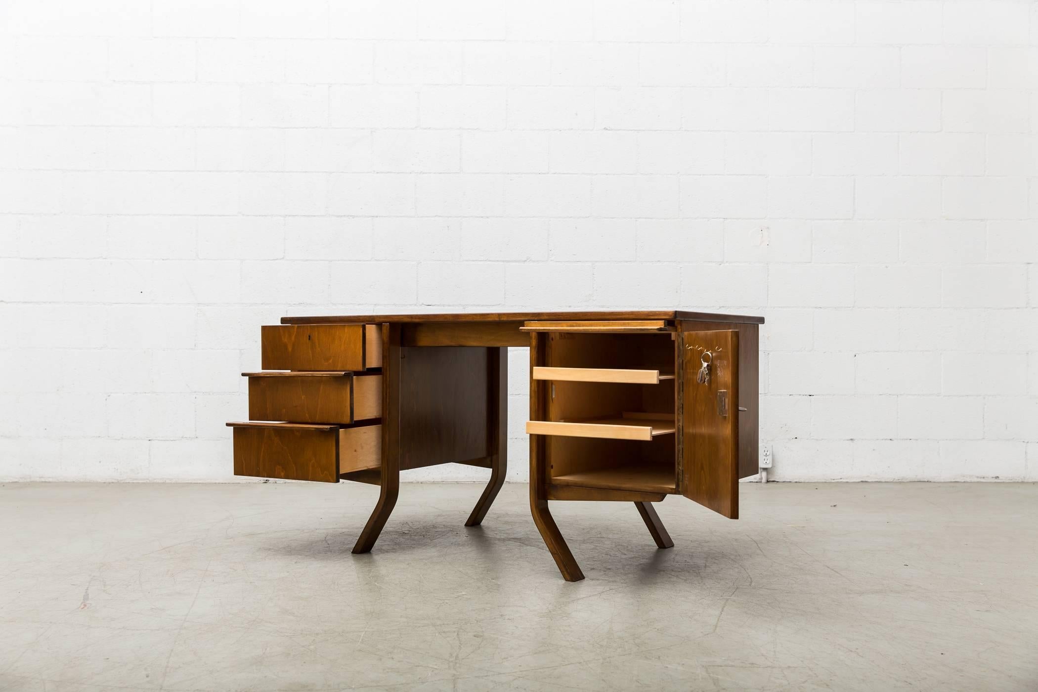 Beautiful midcentury dark stained oak writing desk designed by Cees Braakman for Pastoe. Left side features three sliding drawers with organically carved hand pulls. Right side features large key-entry storage cabinet with sliding sectional pull-out