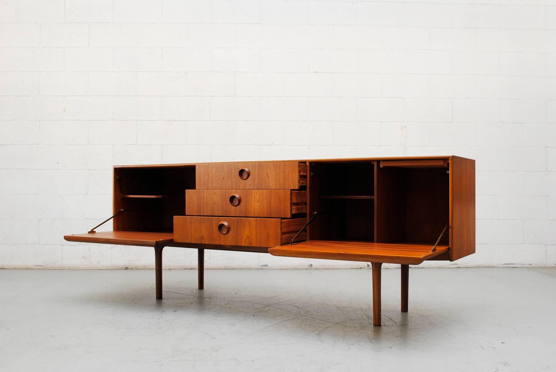 Large sized midcentury teak credenza. Three centre sliding drawers with organically carved round hand pulls. Lined flatware drawer, storage cabinets on either side. Right side pull-out drinks table with printed Formica. Good original condition.