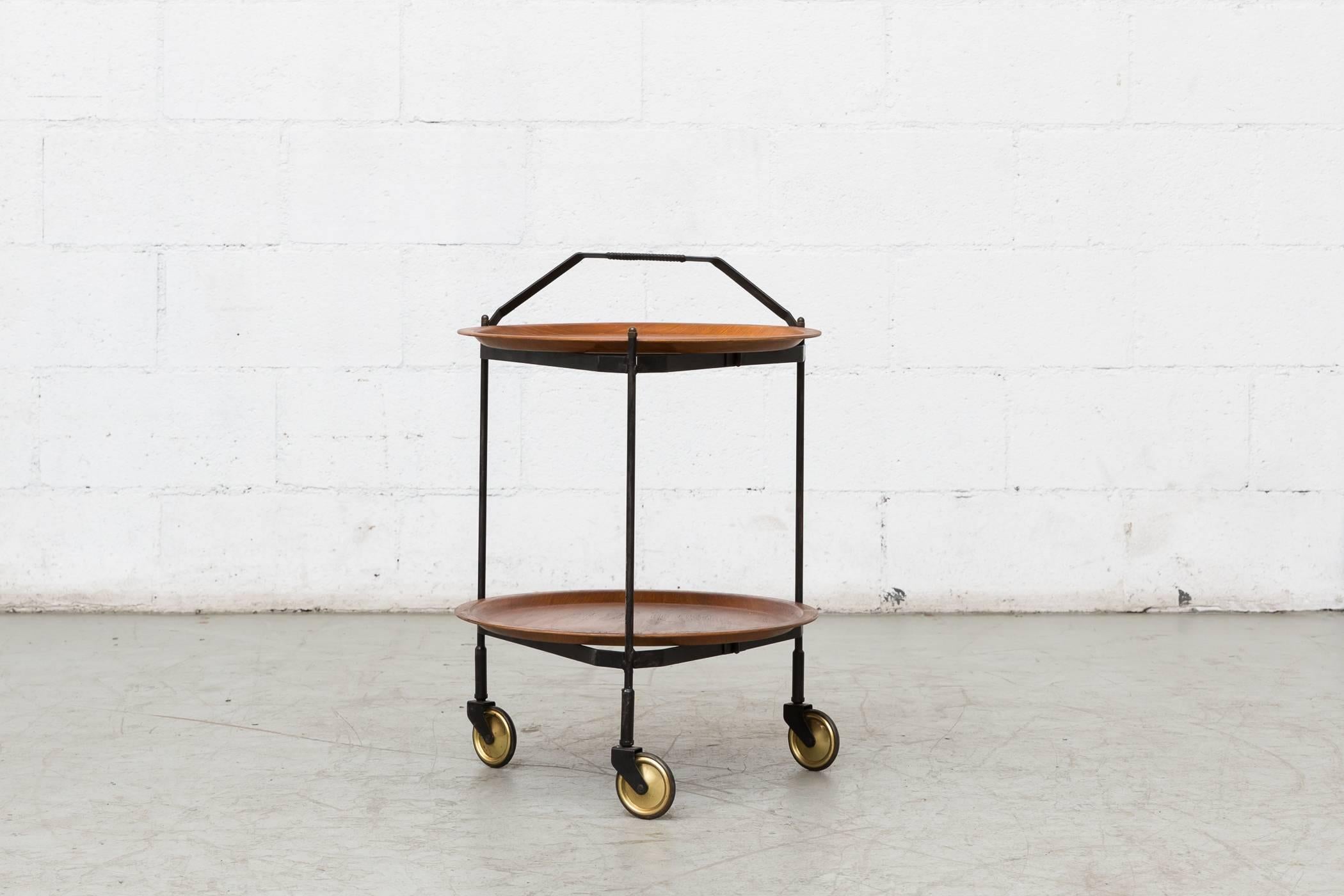 Midcentury rolling cart with two removable teak trays on collapsible black enameled metal frame and leather wrapped handle. Original brass wheels. Leather wrapped handle has been stained black, otherwise original condition.
