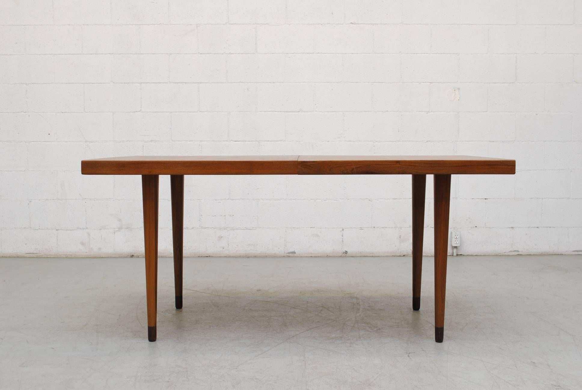 Streamline Danish teak dining table with solid teak tapered legs and hidden extension leaf. In good original condition. Originally low table with removable extensions added. Gorgeous table.
