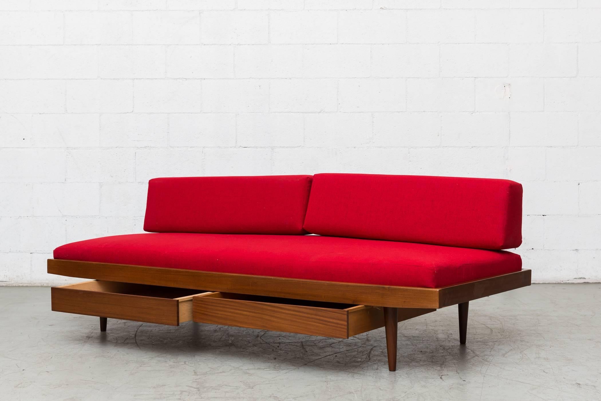 Charlotte Perriand inspired midcentury daybed with tapered legs, double storage drawers and new lipstick red upholstered mattress and bolsters. Has pegboard support. Good original condition, lightly refinished. Others available in different color