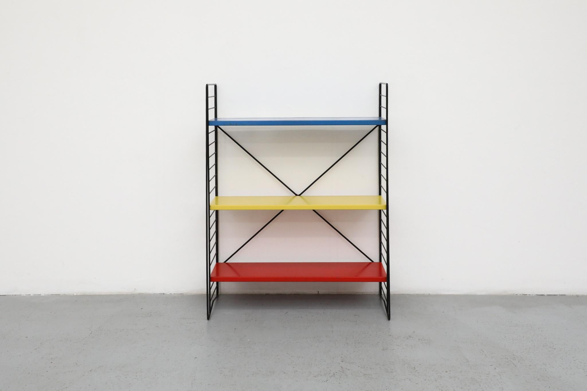 Colorful and iconic, this Industrial standing bookshelf was produced by the famed Dutch manufacturer TOMADO (short for “Tot Aan de Ontwikkeling van Doe-het-zelf Artikelen”) in the 1950s. The bookshelf features three enameled metal shelves in a
