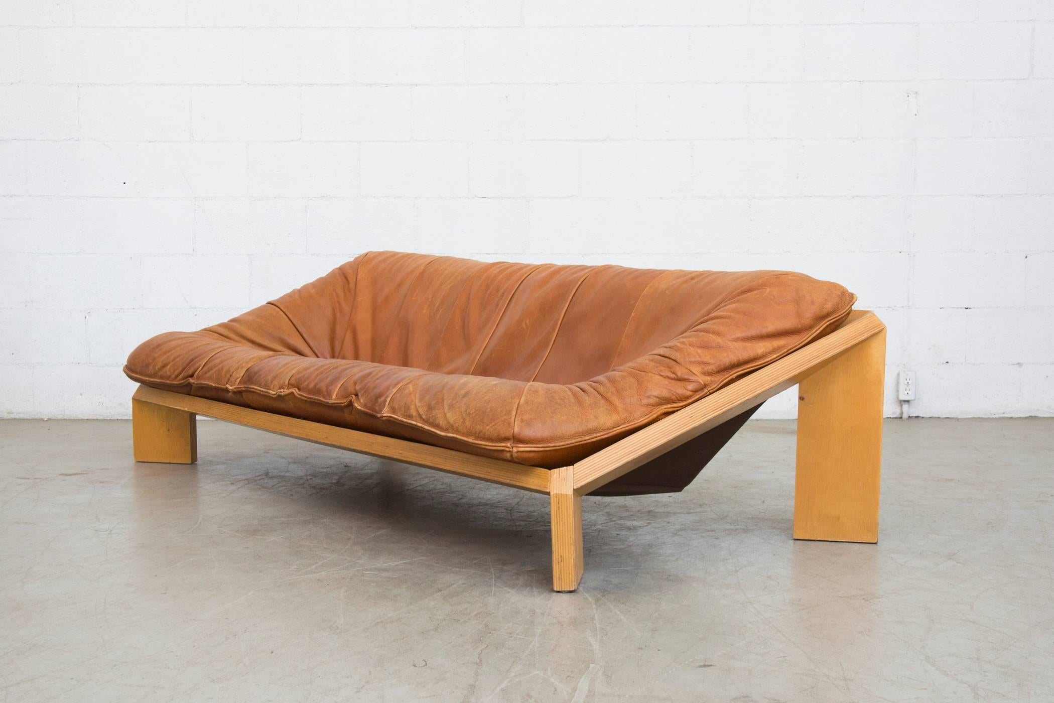 Rare three-seat iconic blocky birch plywood framed sofa with large buffalo leather seat cushion. The leather is incredibly thick and cognac in color with visible wear and patina, some scratching visible to seating and frame. In good original