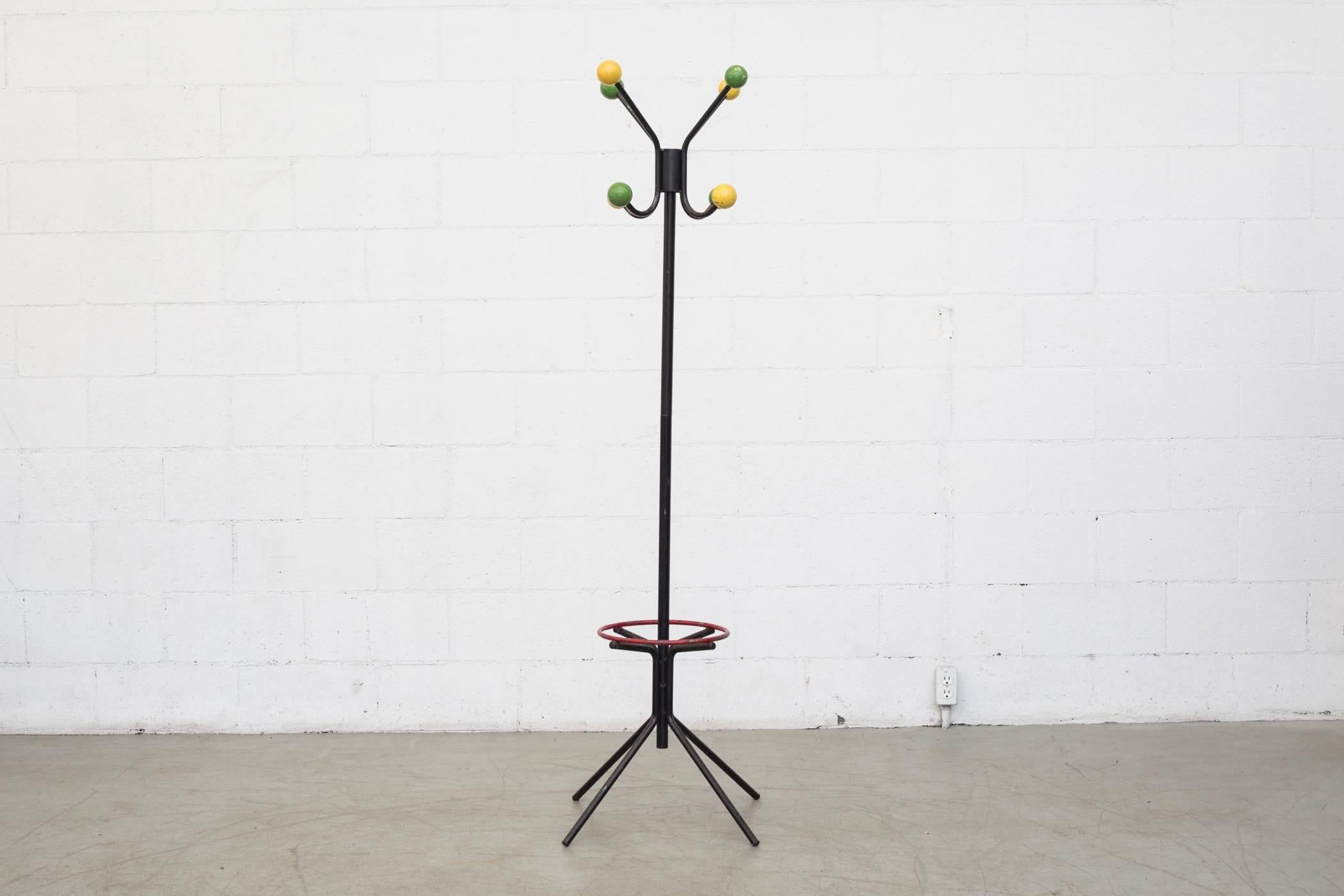 Black enameled metal coat rack with colored wood balls and red enameled metal ring for umbrellas. The pole can be detached. Original condition with visible patina and wear.
