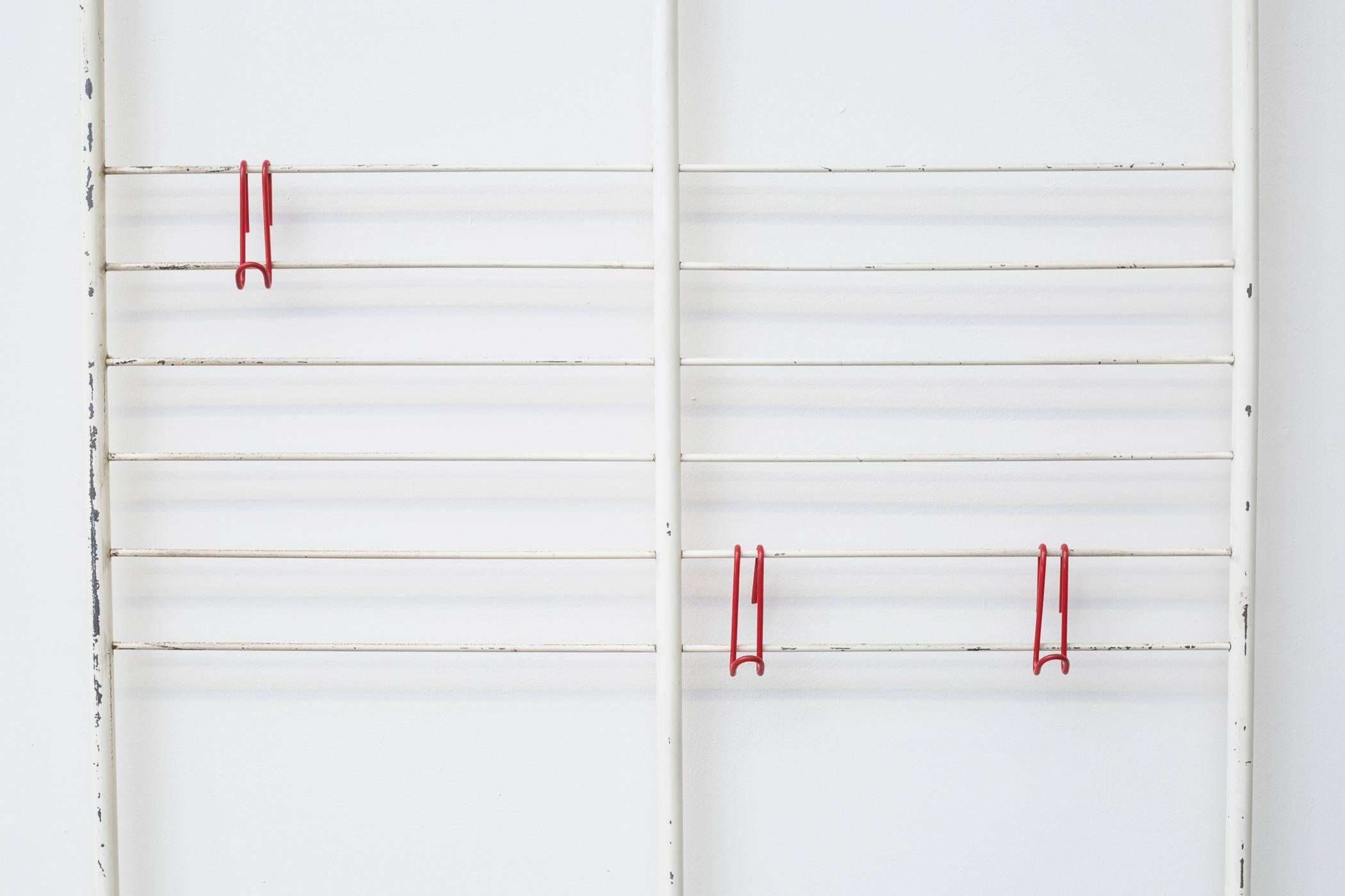 Bone white enameled metal wall mount coat rack with removable hat shelf and five decorative red wire hooks. In very original condition with visible signs of wear. Some paint loss.