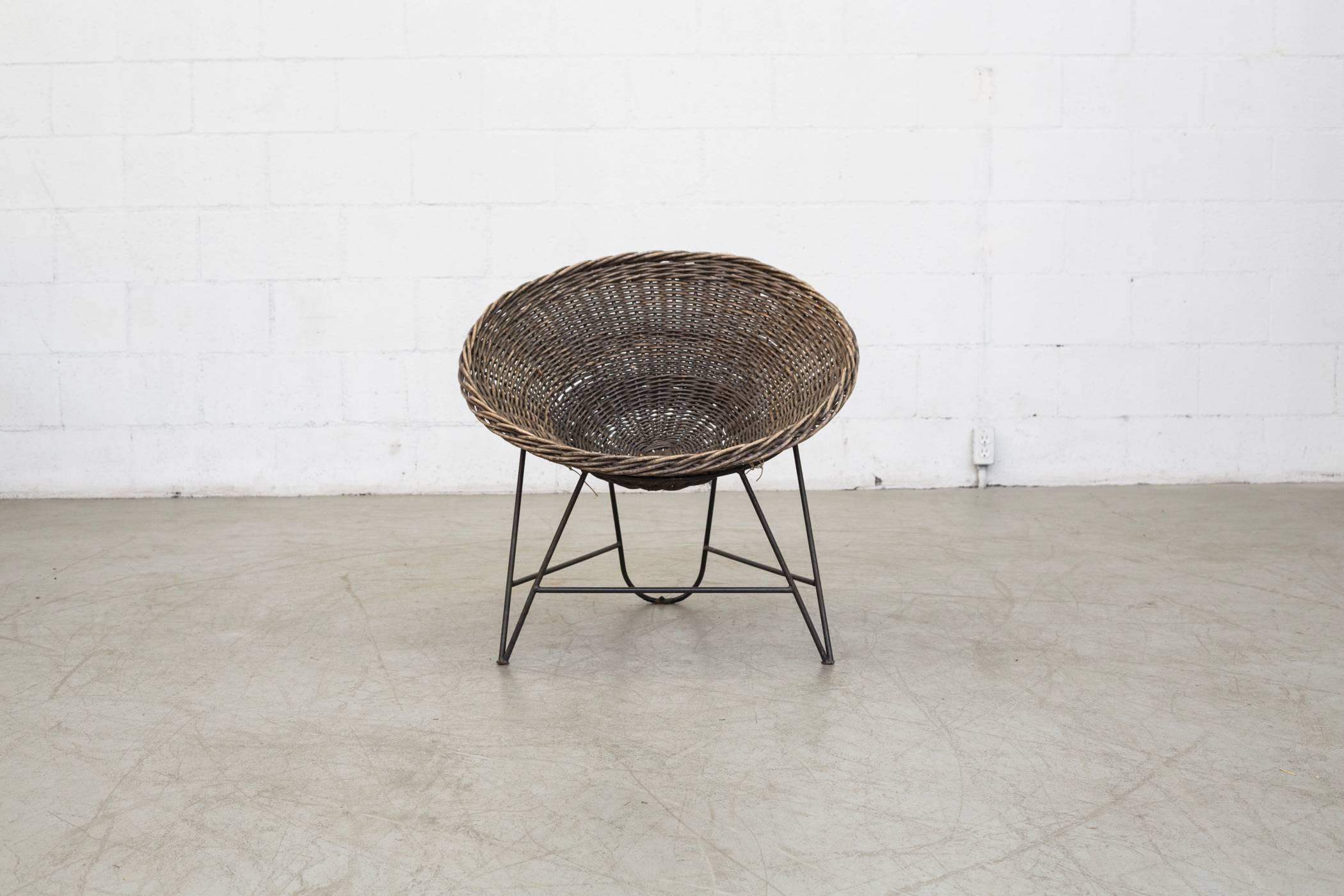 Beautiful woven bucket seat with visible fading and patina that sits in a black enameled metal base, also with visible wear and patina. Minimal rattan loss.