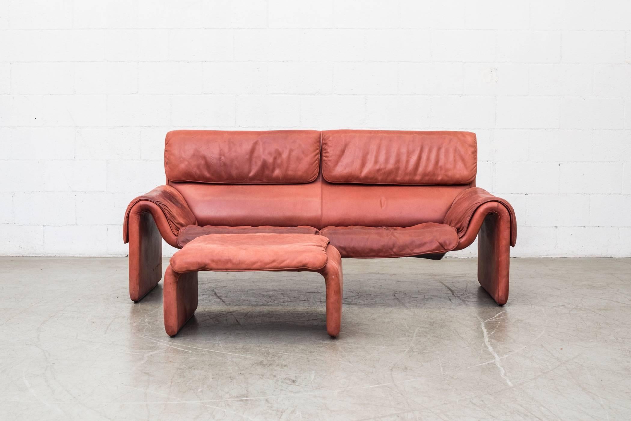 Soft leather sofa with matching ottoman in salmon color by Elastoform. Original condition with visible wear and staining consistent with its age and usage. Ottoman measures 27.5 x 25.5 x 14.5. Sold as set.