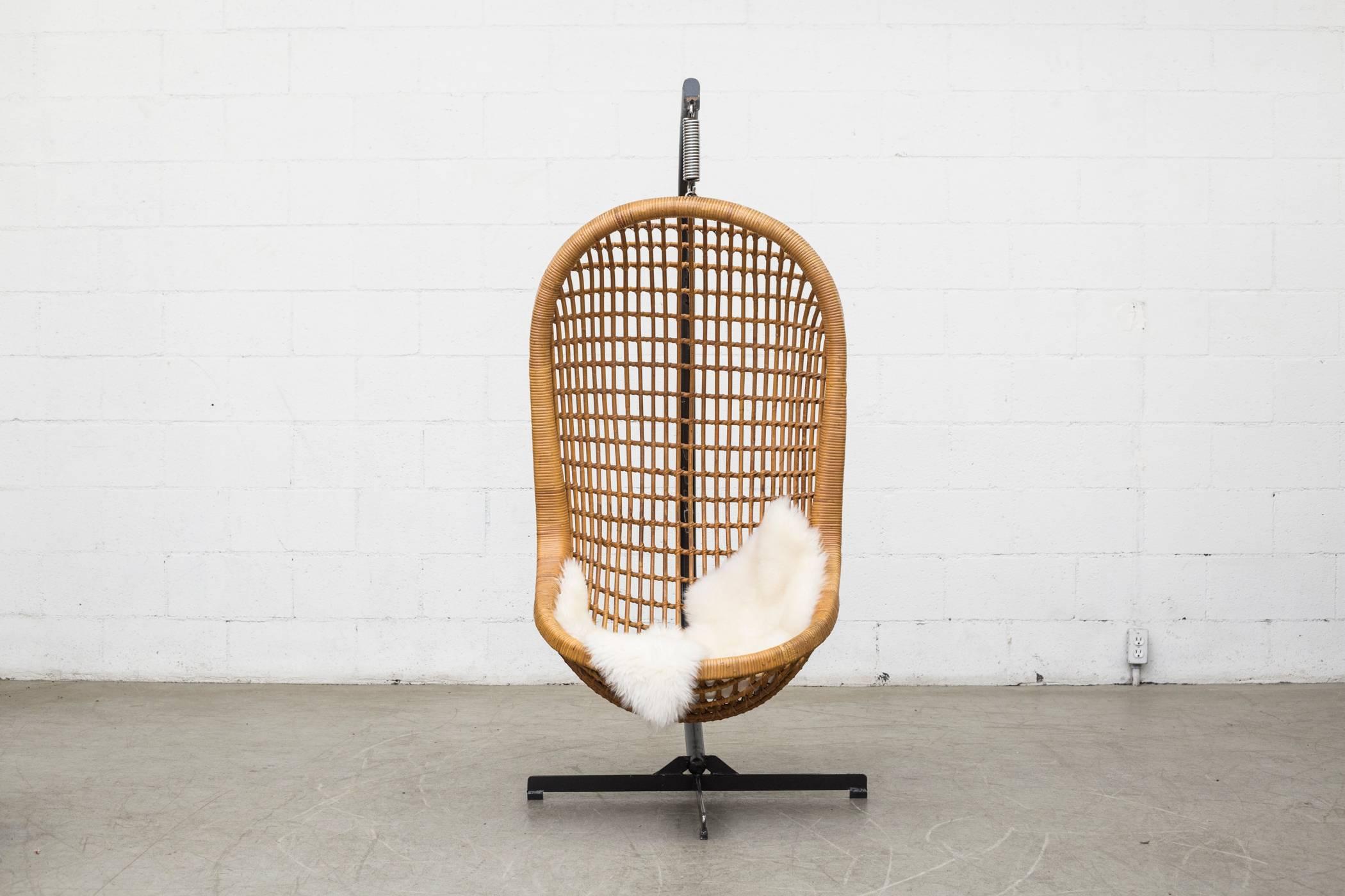 Straight from 1970s heaven. Beautifully woven rattan free-hanging basket chair. Held by heavy black enameled metal base with spring support. Estimated to hold about 200 pounds of weight. (Sheepskin not included).