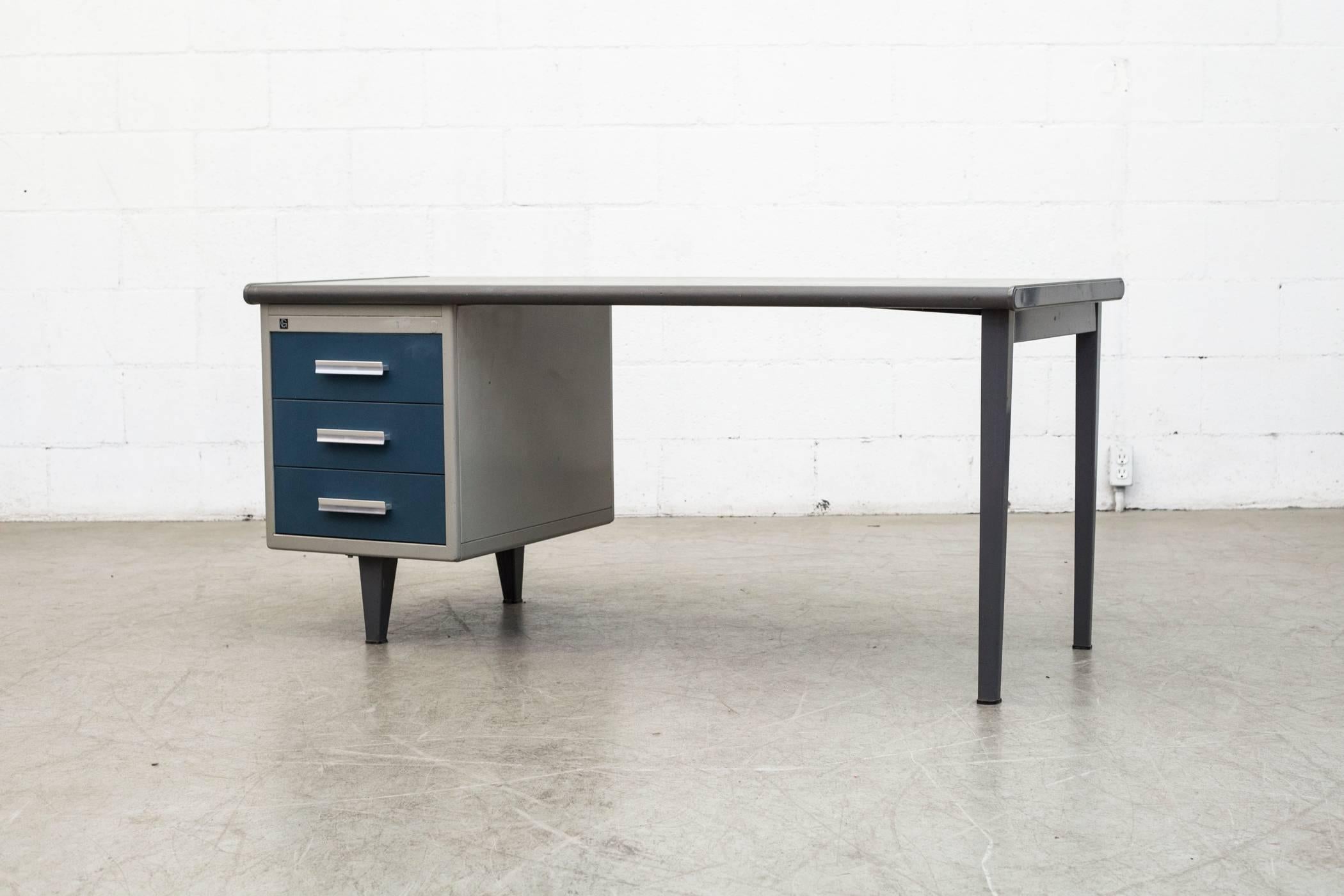 An eyecatcher. This long and low Mid-Century Industrial metal desk by Dutch Design Company Gispen has blue enameled pull-out drawers with cast aluminium pulls and a grey enameled frame charcoal linoleum top. Item is in original condition.