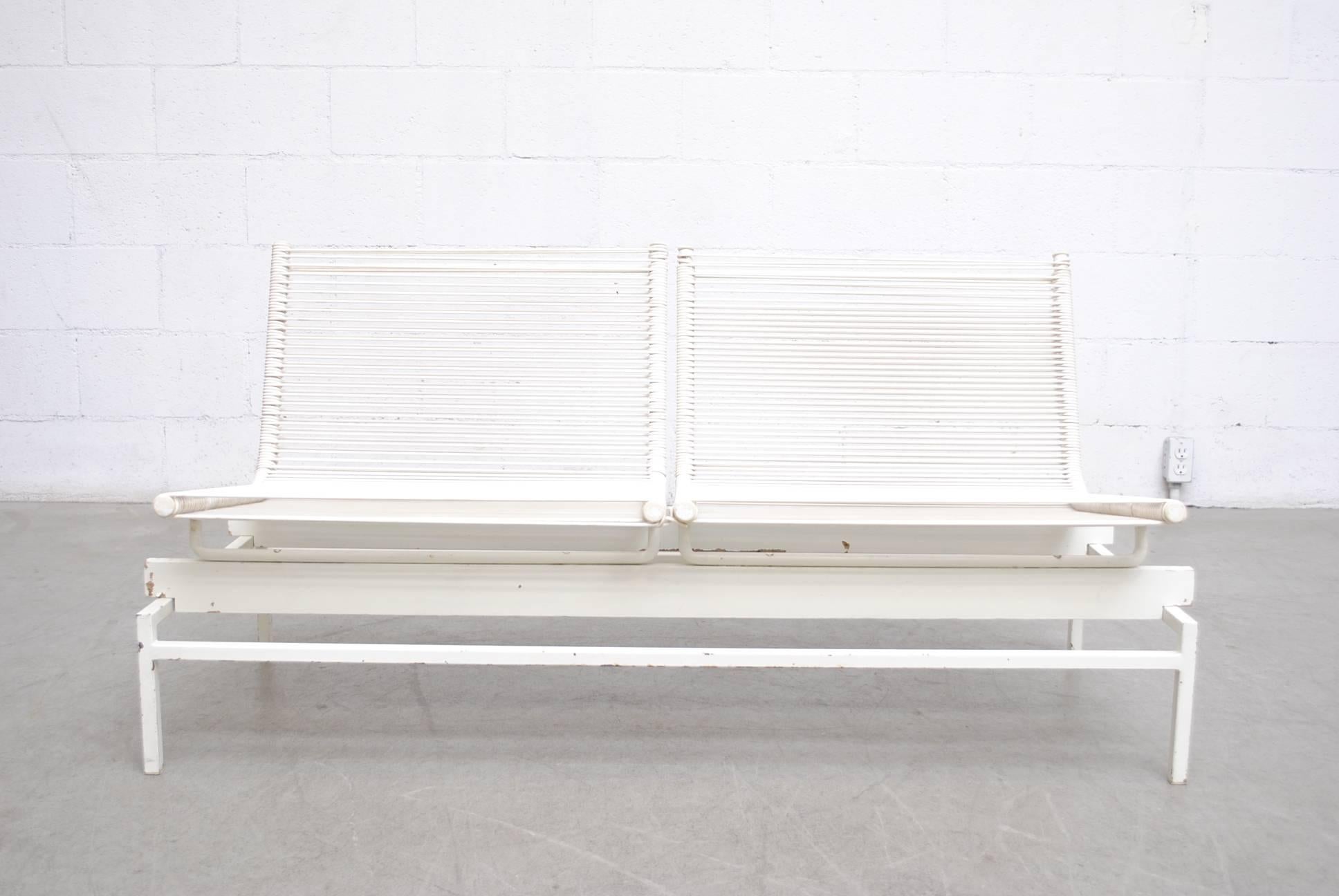 Two-seat bench with white enameled metal frame and string seating. Some paint and enamel loss, visible wear consistent with its age and usage.