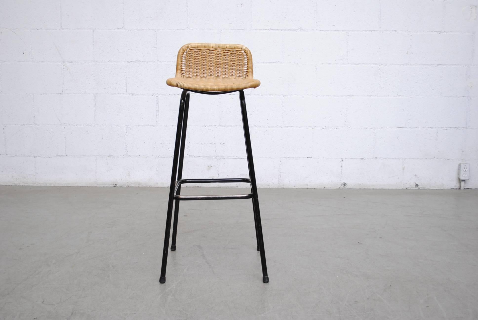 Charlotte Perriand style bar stools with woven rattan seating with black enameled tubular frame, in original condition with visible signs of wear. Other similar stools available but listed separately