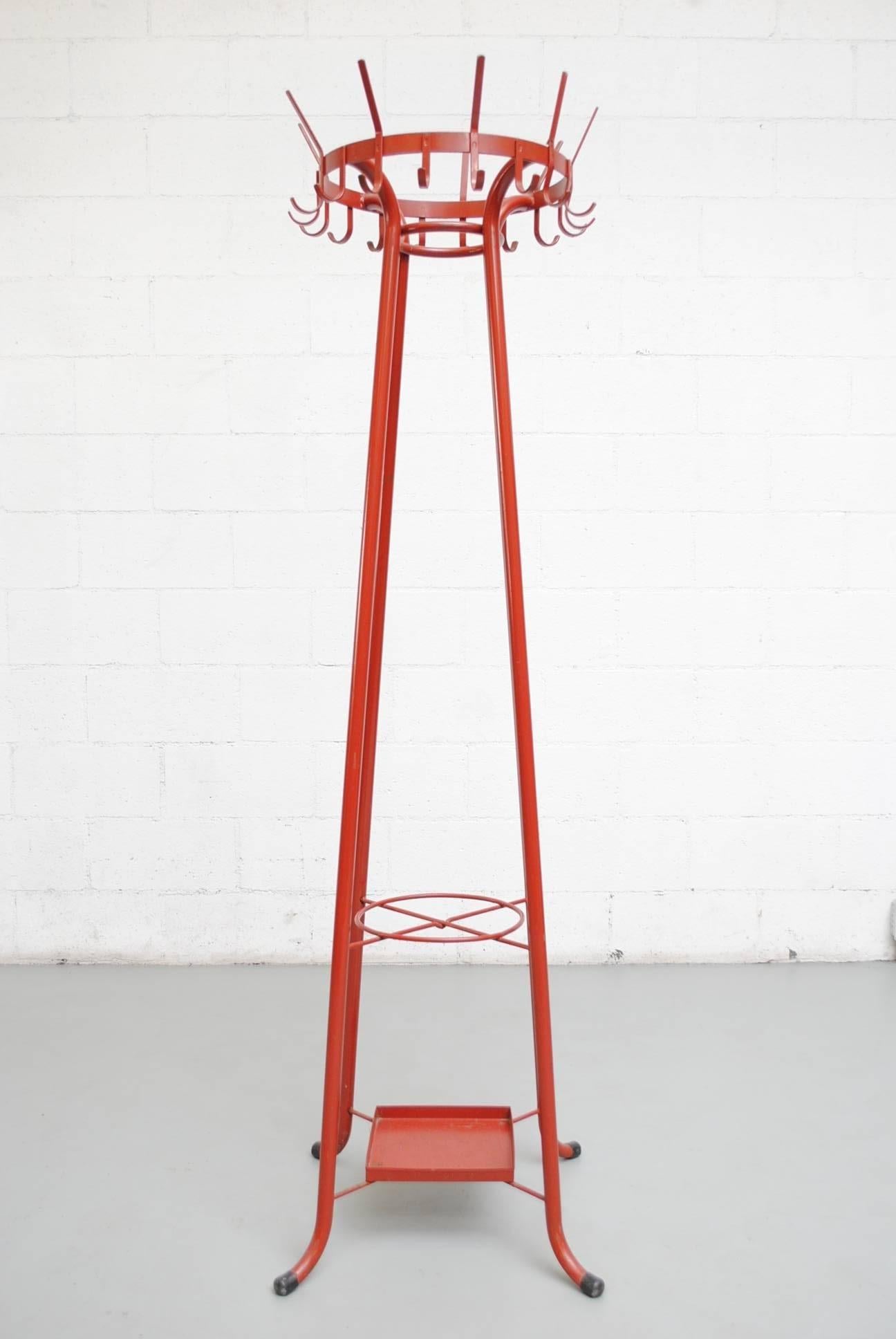 Bright red enameled metal institutional standing coat rack with built in umbrella stand. Impressive design and color. In original condition with visible wear consistent with its age and usage.