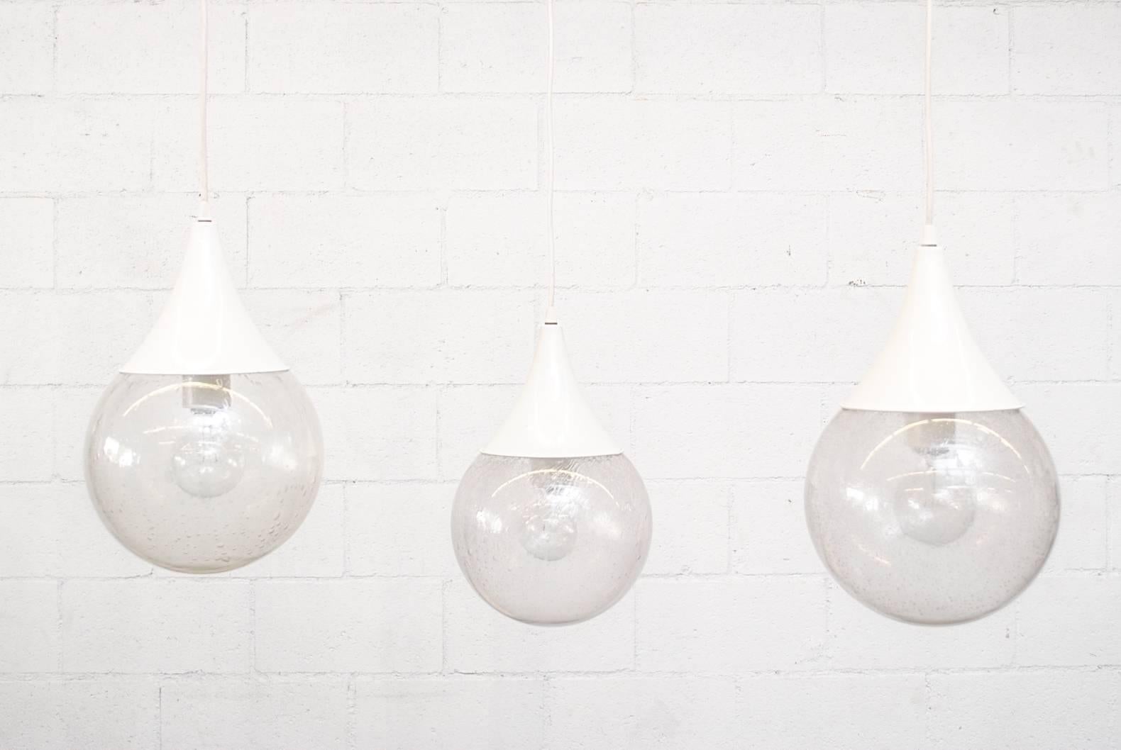 Colgantes en forma de lágrima, estilo RAAK, de mediados de siglo, con globo redondo de cristal burbuja y herrajes de metal esmaltado en blanco. Las luces están en su estado original, con un desgaste visible acorde con su edad y uso. Precio