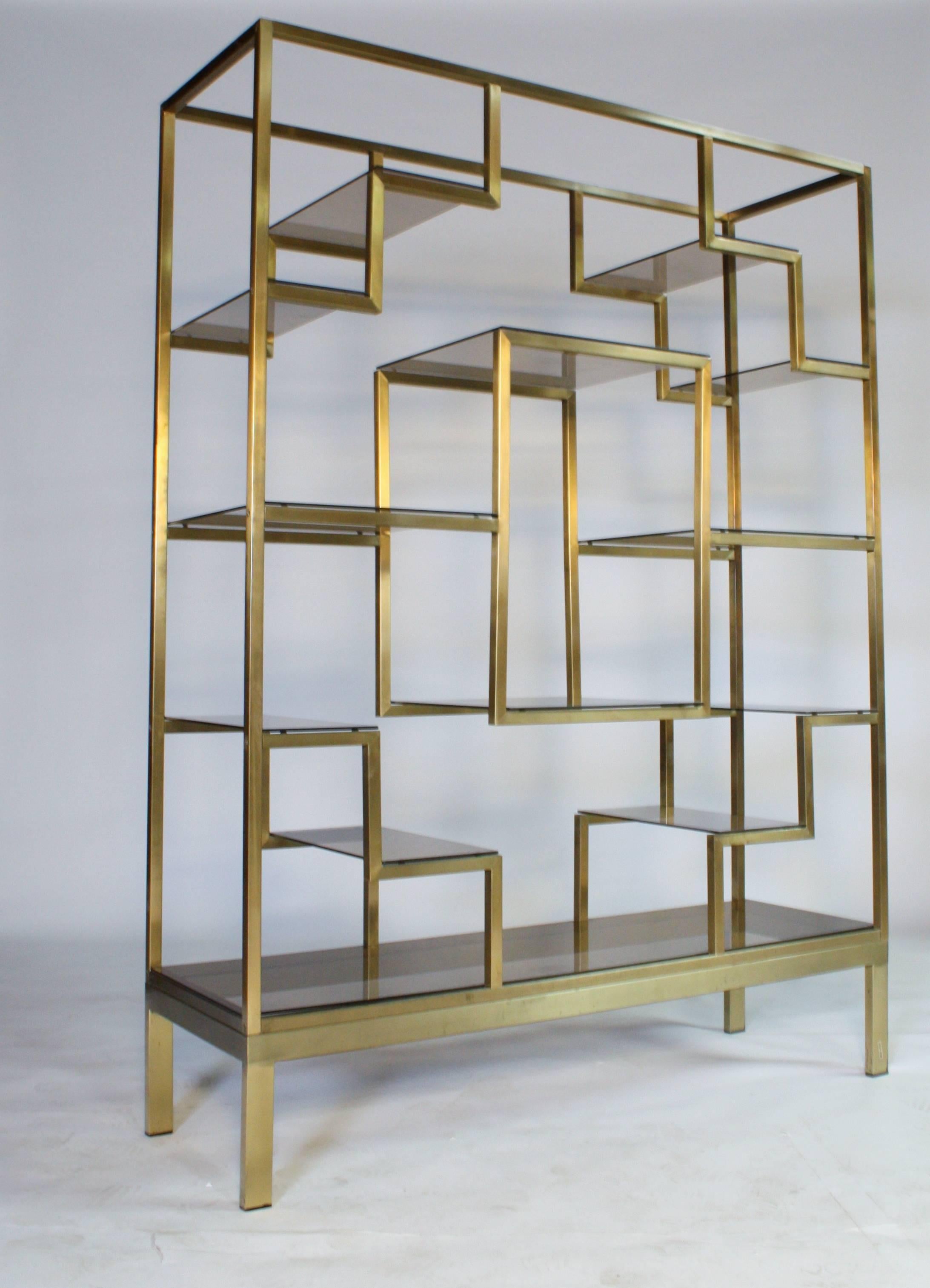 Brass and smoke glass etagere in a beautiful brushed gold finish attributed to Romeo Rega made in Italy (labelled). 13 glass shelves all in excellent condition with the exception of one small flea bite on the bottom shelf (barely noticeable).