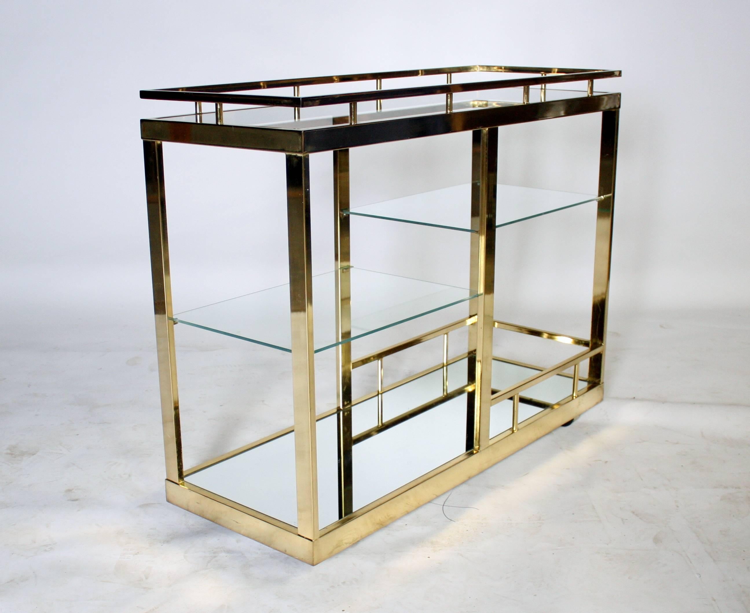 Mid-Century four-tiered brass bar cart. Bottom shelf has a guard rail for bottles on one side and a full mirrored shelf. Two-stacked half shelves in glass and a full glass top shelf complete this large scale brass cart on castors.