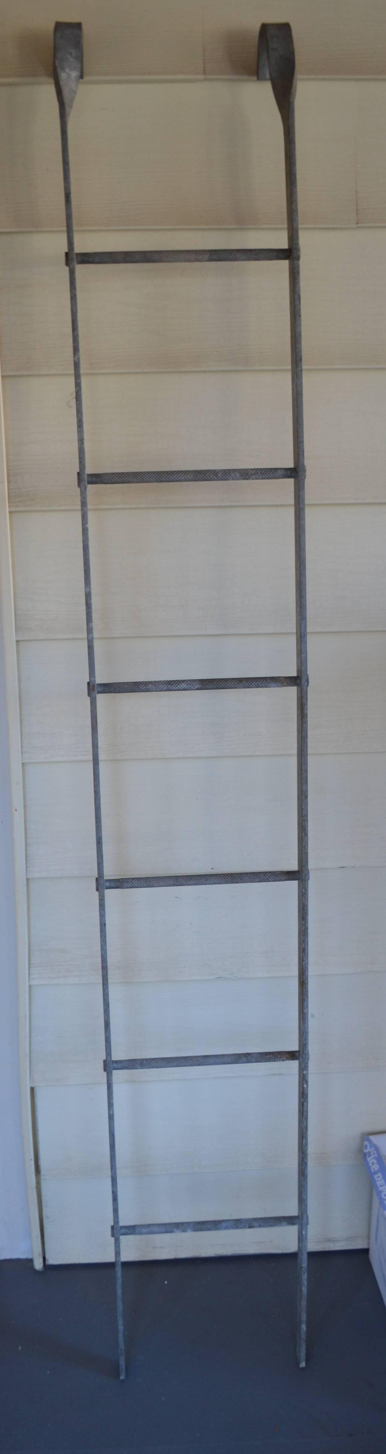 Ladder of galvanized steel with top hooks was used as fire escape or in factory or in store and library for shelf stocking. Note the heavy duty foot grips on each rung. Clean and striking in blue toned steel. Use to display strings of lights or as a