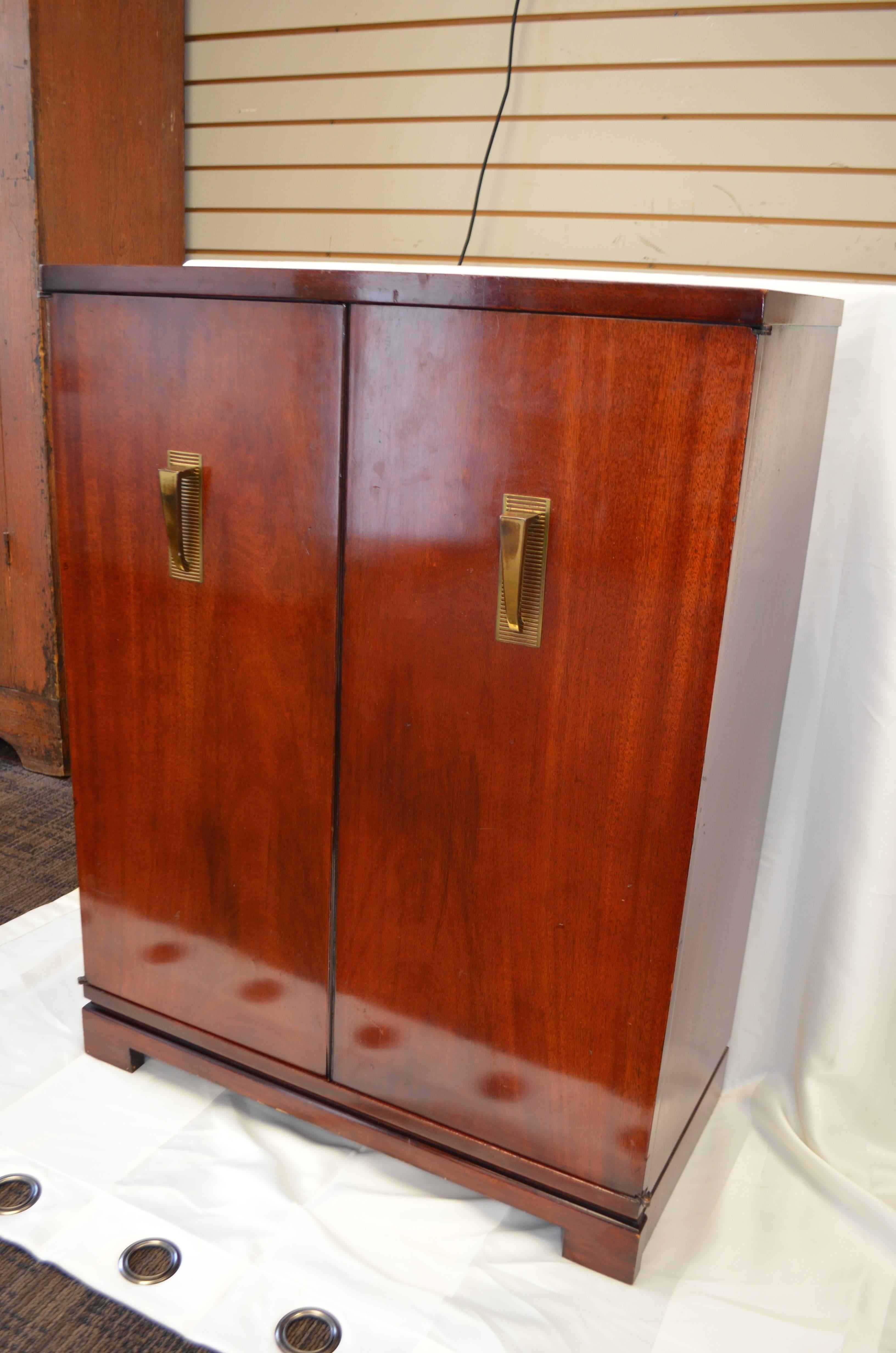 Mid-Century bar or storage cabinet with two doors, brass Deco pulls and two fixed interior shelves. High gloss, mahogany veneer gives the piece sharp, glamorous appeal. Solidly built with sturdy shelving and double doors that snap closed with