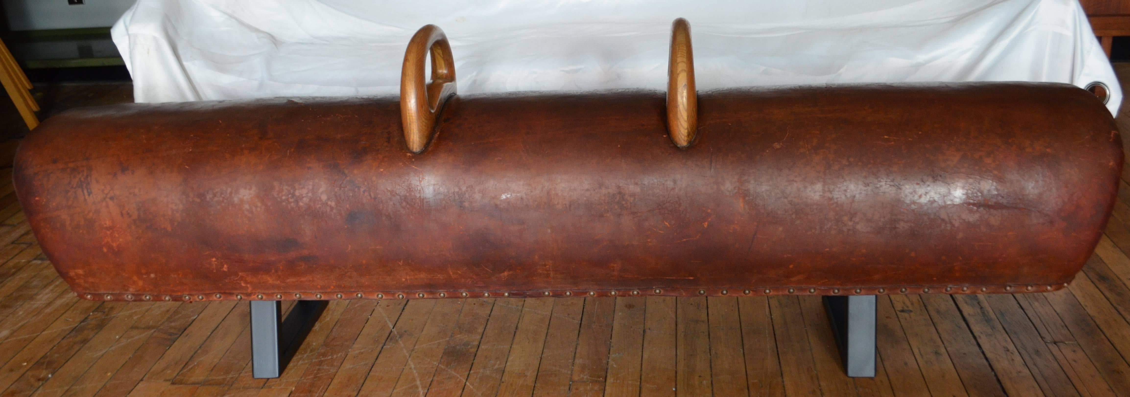 Gymnast leather pommel horse has been transformed into a bench with steel bracket legs painted black. Striking bench for hallway or entranceway or overflow seating. Beautifully-worn leather has been cleaned and conditioned displaying dramatic color