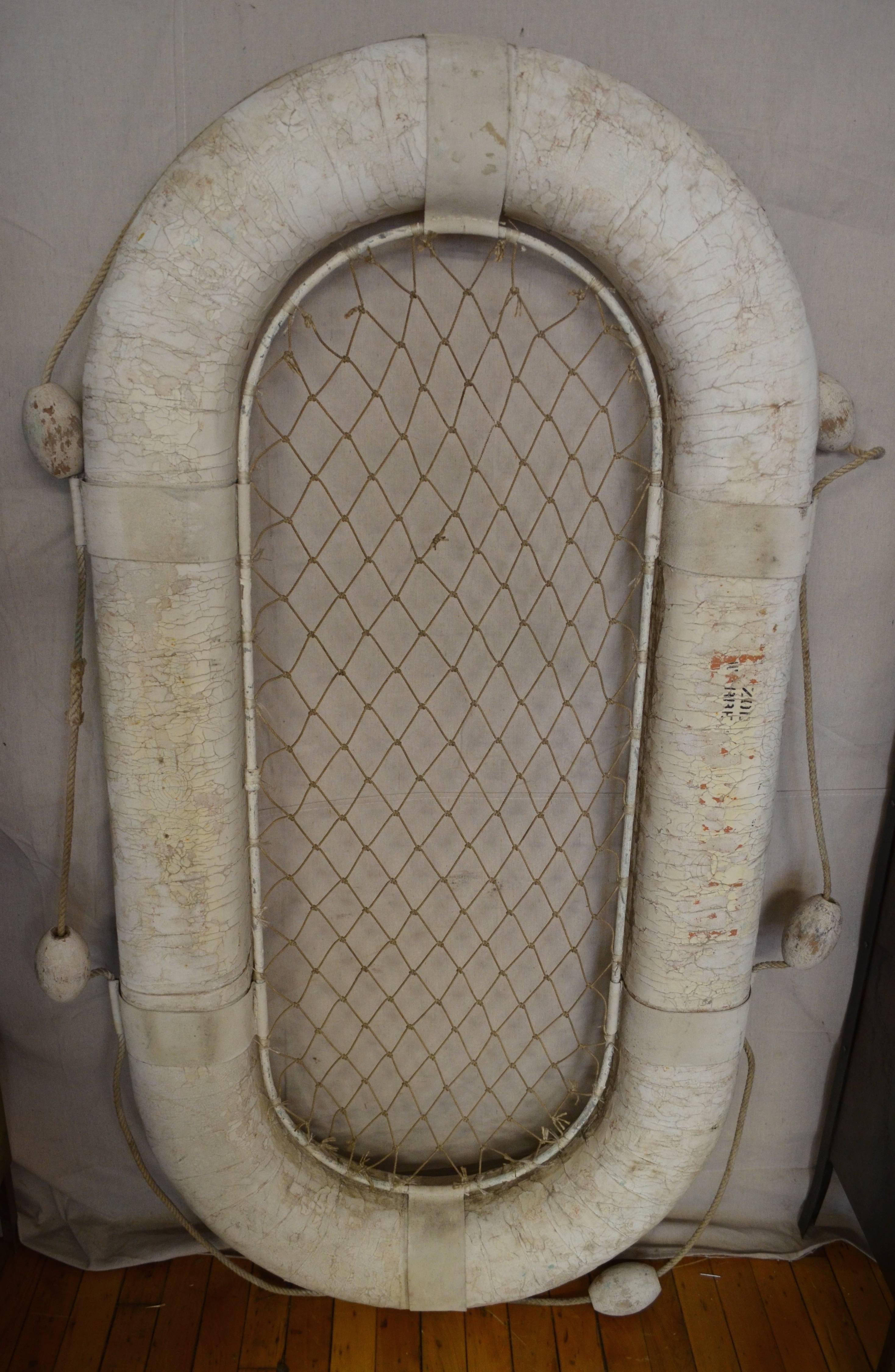 Raft utilized on a naval ship for rescue at sea. White-painted canvas with wooden floats and rope mesh interior. Reputed to be from the 1940s, this rescue raft may well have seen duty aboard ship in the South Seas during WWII. Sea weather has made a