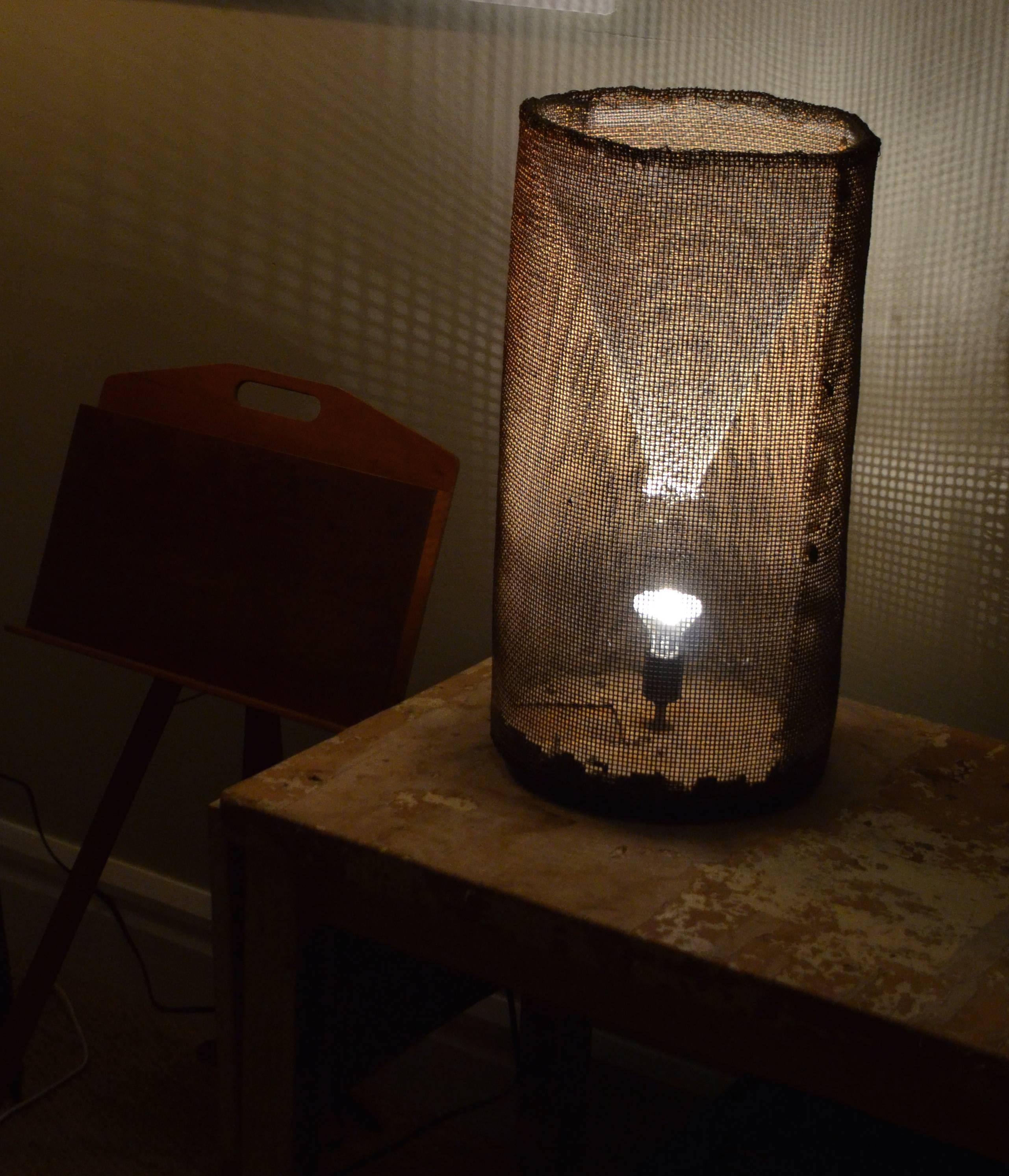 Fish trap of richly-rusted steel mesh wire has been made into an ambiant light for table or floor, mounted on wooden ball legs. A mysterious glow emanates from within while casting a shadowy matrix on surrounding walls. Lead photo (above) was taken