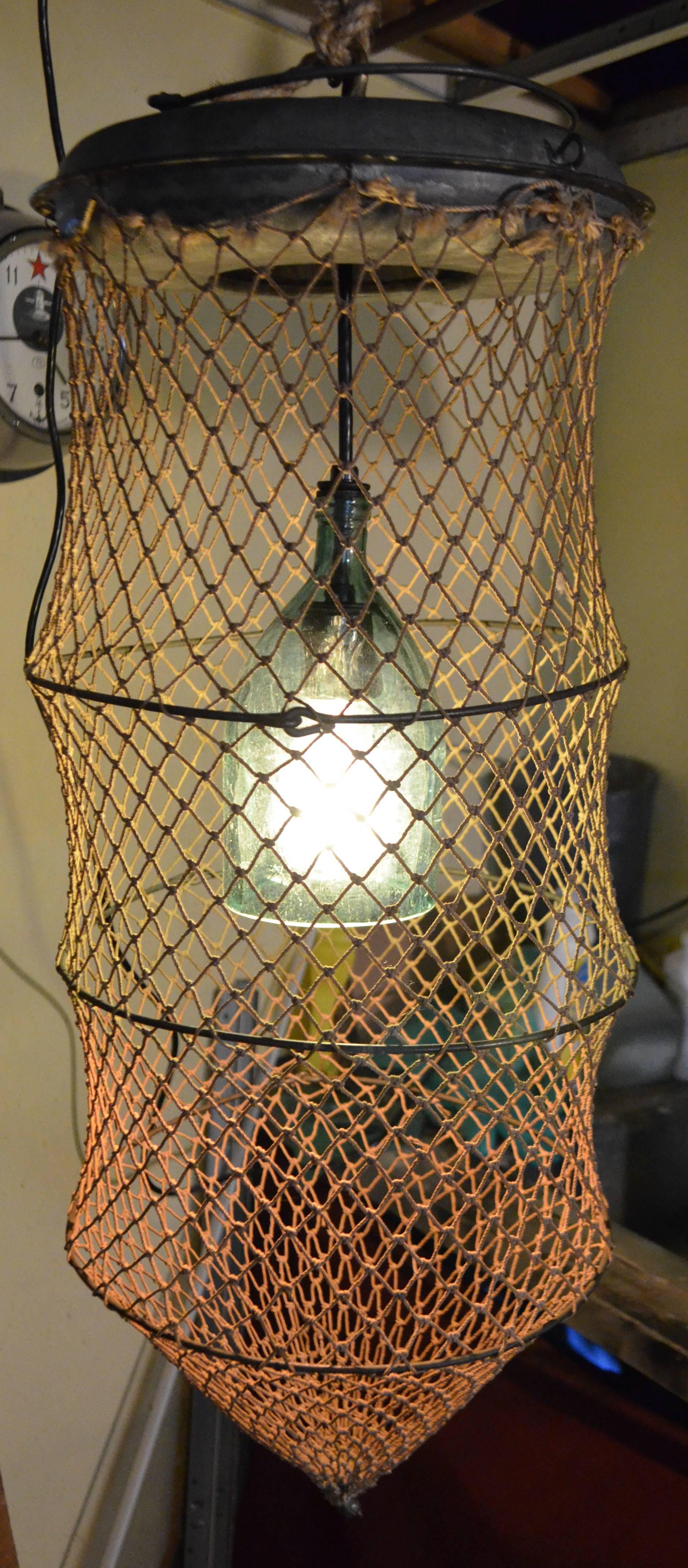 Pendant light created by mounting European seltzer bottle within a seine net fish trap. Casts a wonderfully ambient light and the colors of the netting shading from red to green to taupe. Professionally wired with porcelain socket and pendant wire