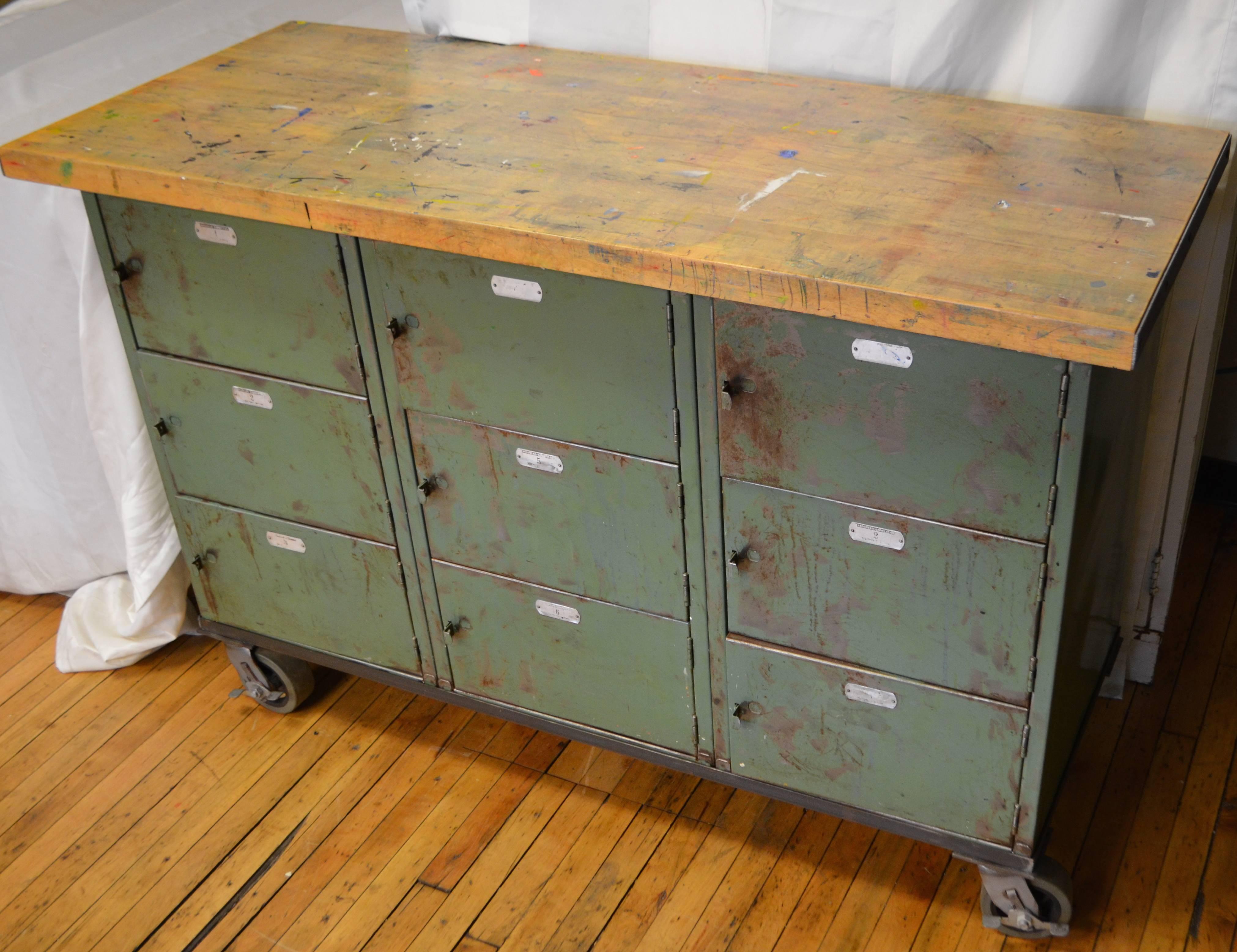 Cabinet with maple worktop found in art school is on locking wheels with nine numbered storage compartments. Piece has been cleaned and sealed, including the top with paint marks and splotches left intact from student art work. Highly versatile with