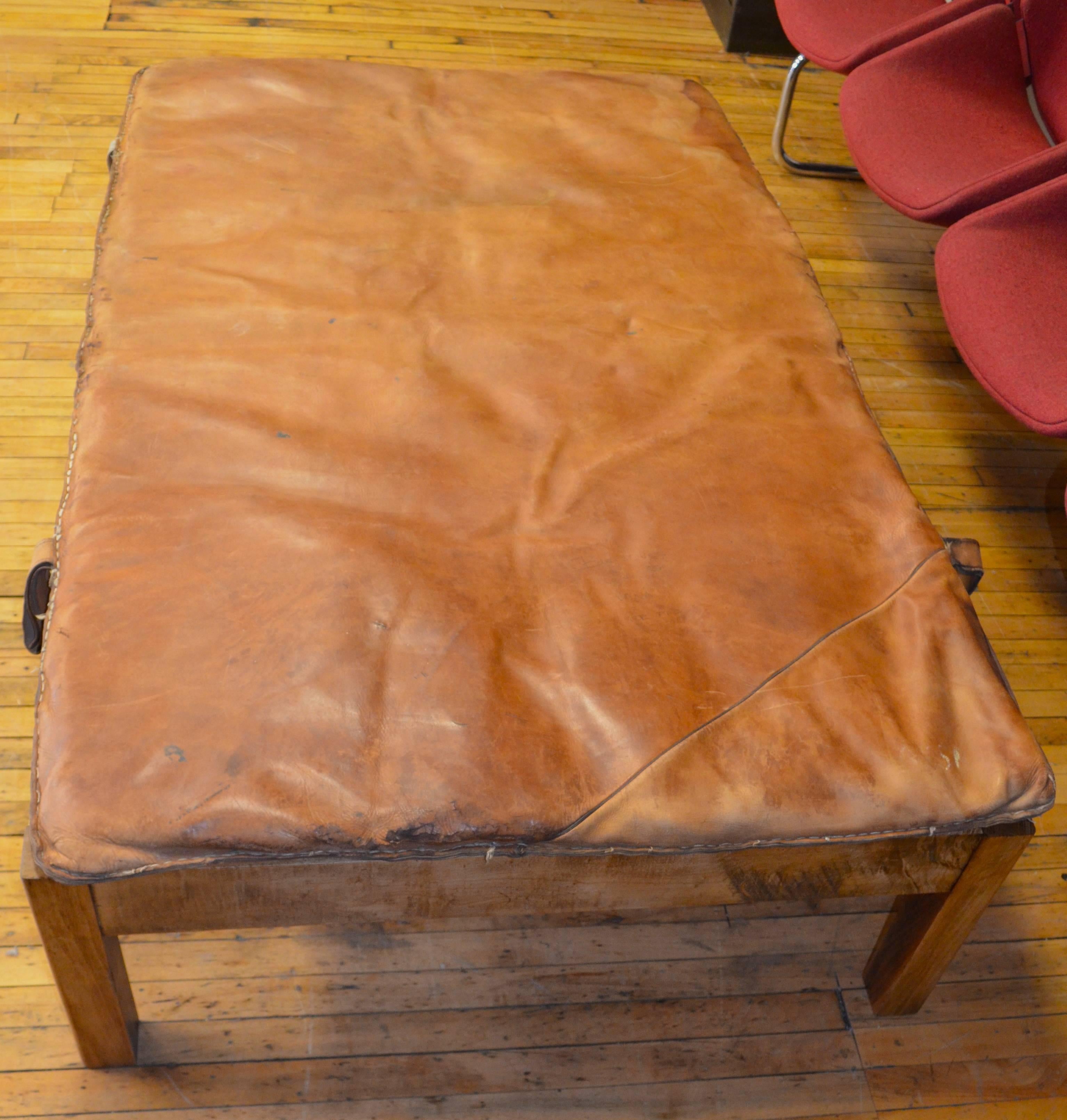 Coffee table or ottoman of vintage leather gymnasium mat with canvas straps atop handcrafted wooden frame. The hand of the leather is exquisitely soft with wear. The frame with mat is so sturdy you can dance on it, sleep on it, rest your tired feet