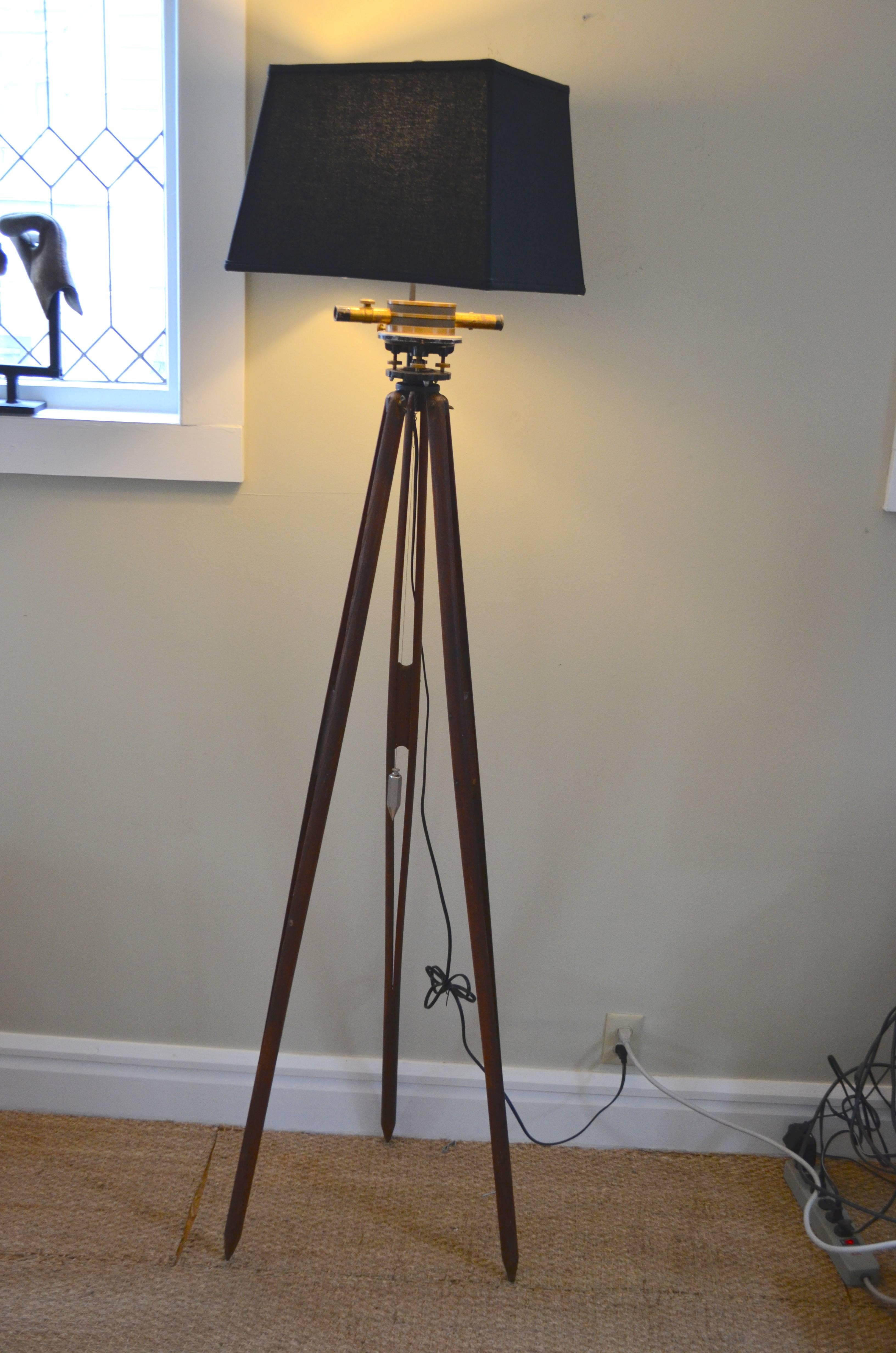 Floor lamp from surveyor's tripod includes brass telescope and hardware including internal level, external leveling screws as well as steel plumb bob. Striking piece that's been professionally wired with 10-foot black cord, three-way socket, 8 inch