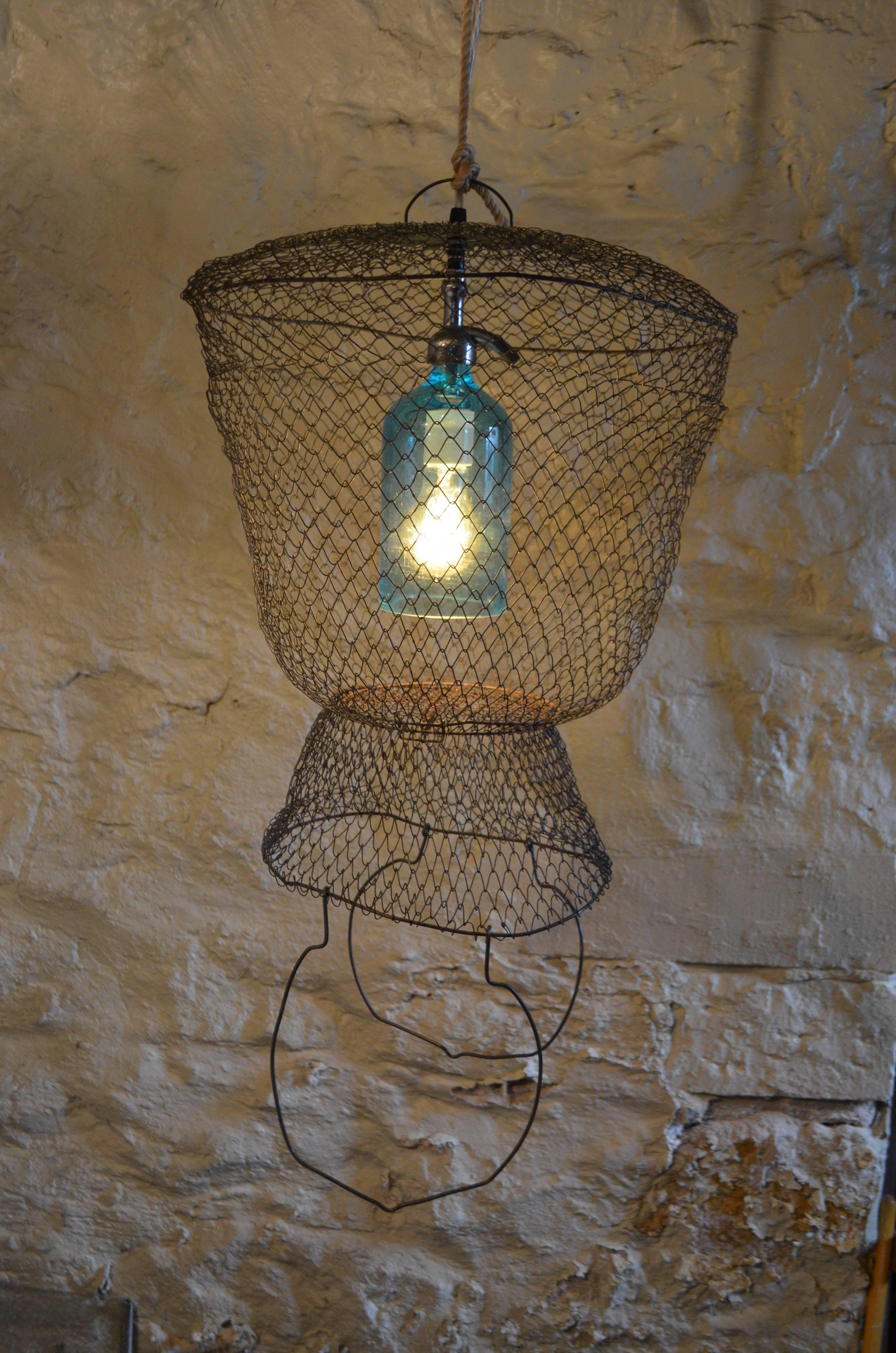 Pendant light from a sea blue, New York etched seltzer bottle suspended inside a steel mesh fish basket from France. Just in time for the summer home on the ocean, lake or at your wooded retreat. Wonderfully soft ambient for porch or patio and those