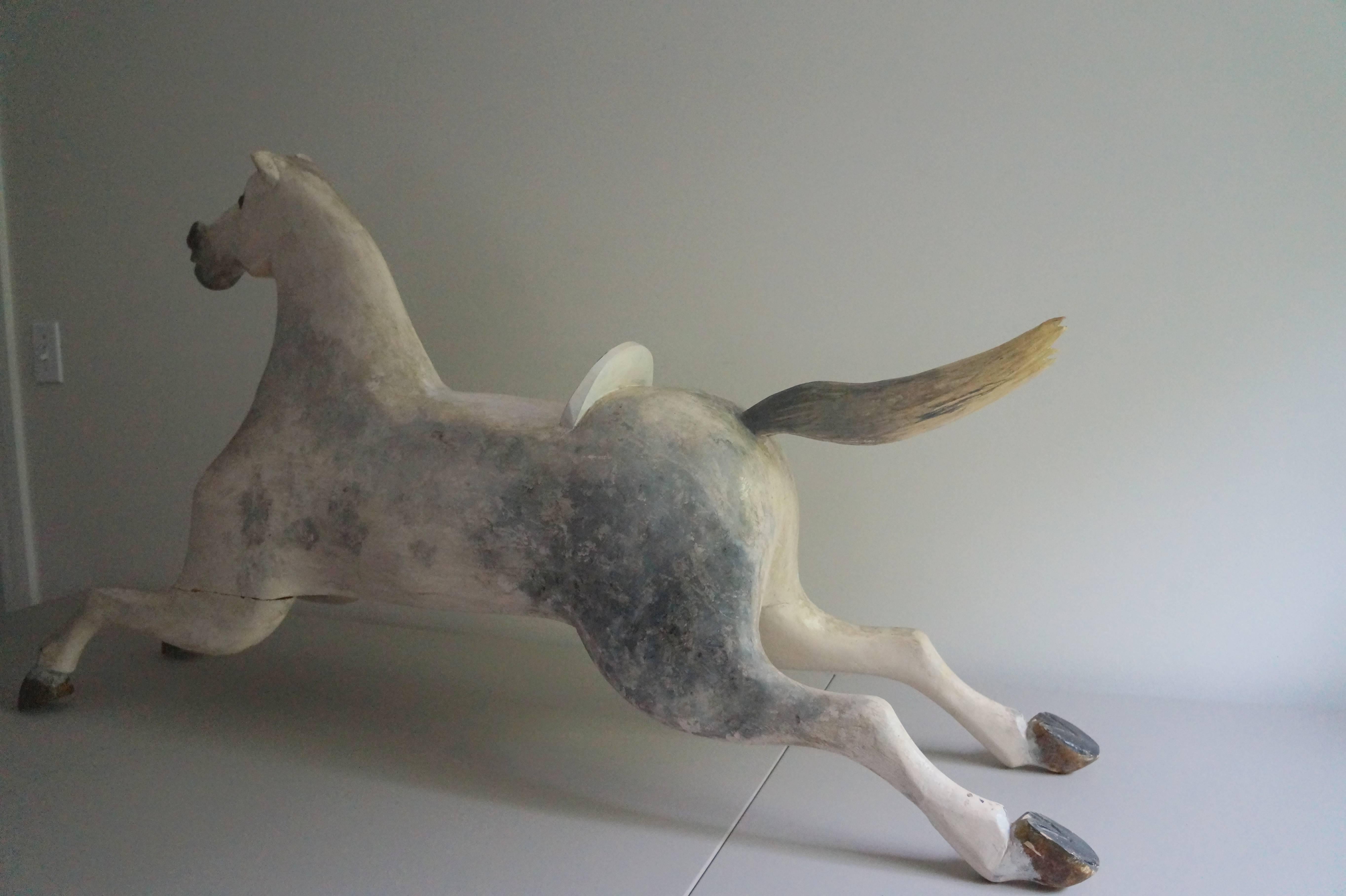 19th century wood horse, 50 inches long. Originally sat on a glider. Hand-carved with glass eyes. This one is a bit unusual as he has a wood tail. Not his original paint; however, the original paint may be underneath. Chips on tips of ears and a