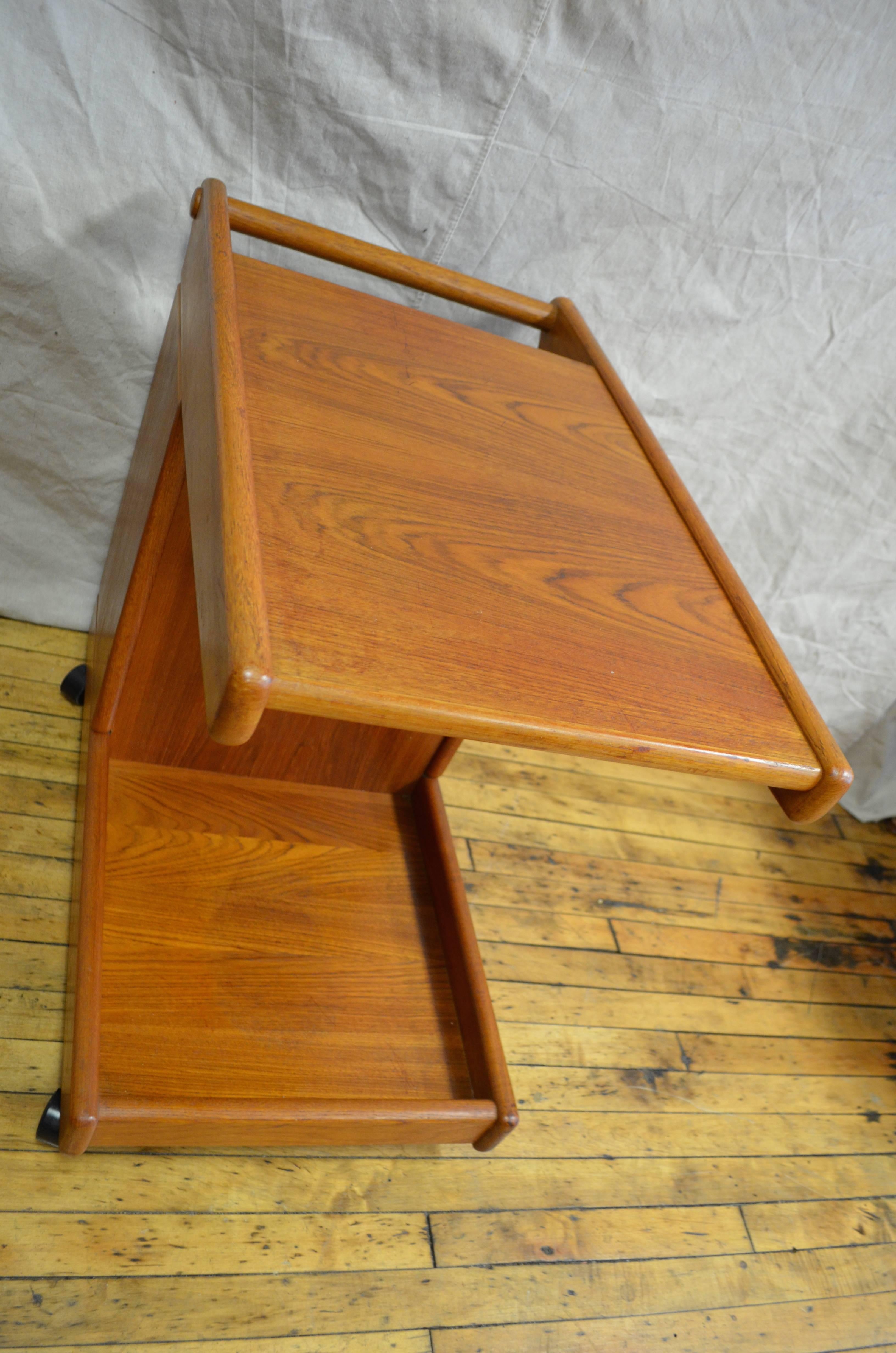 Simple, speed Mid-Century bar cart of teak on wheels with handle and two levels.