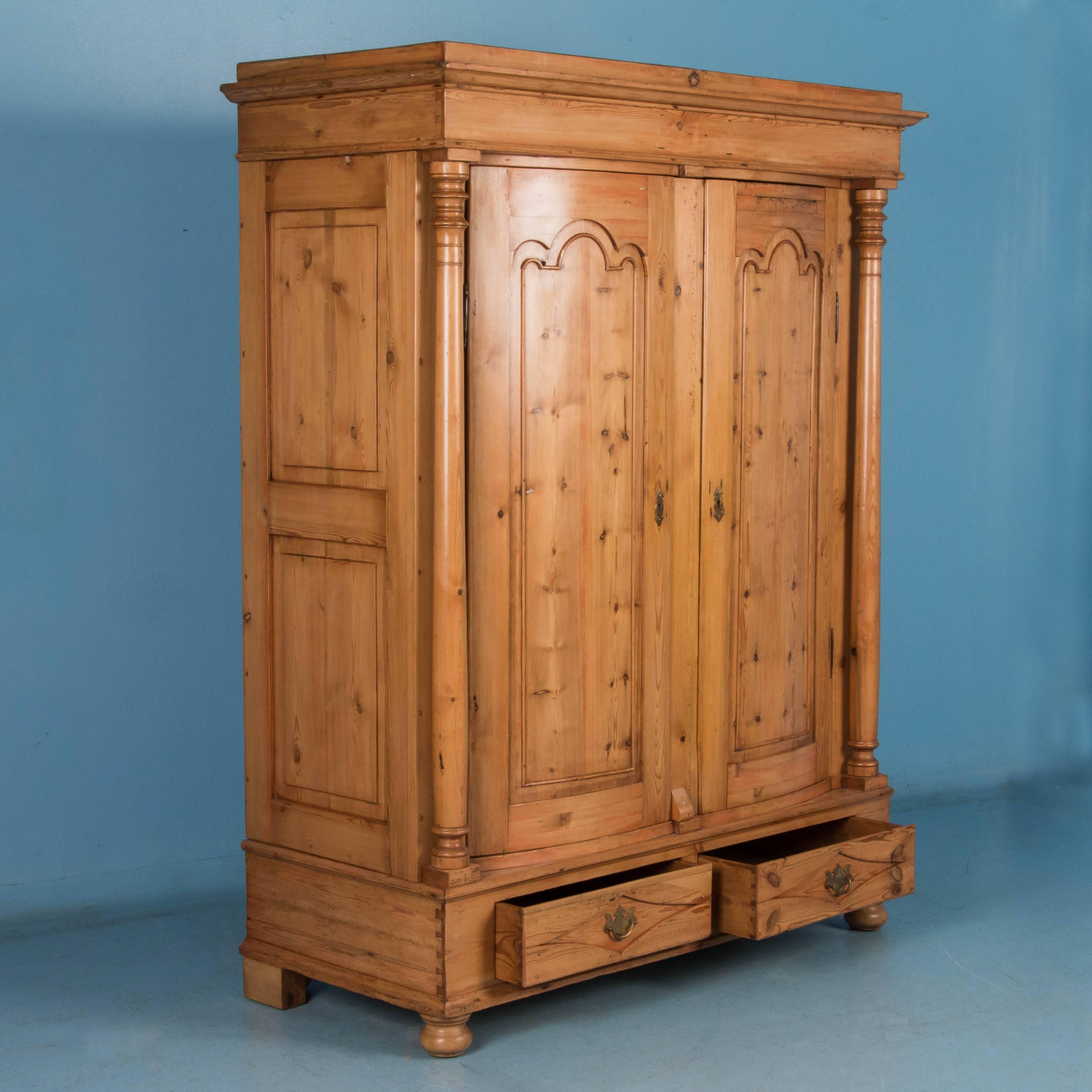 The striking beauty of this large country pine armoire is due to the graceful lines and curves enhanced by the warmth of the natural pine and faint hints of old red paint. Seen from any side, this armoire attracts the eye. This Biedermeier period
