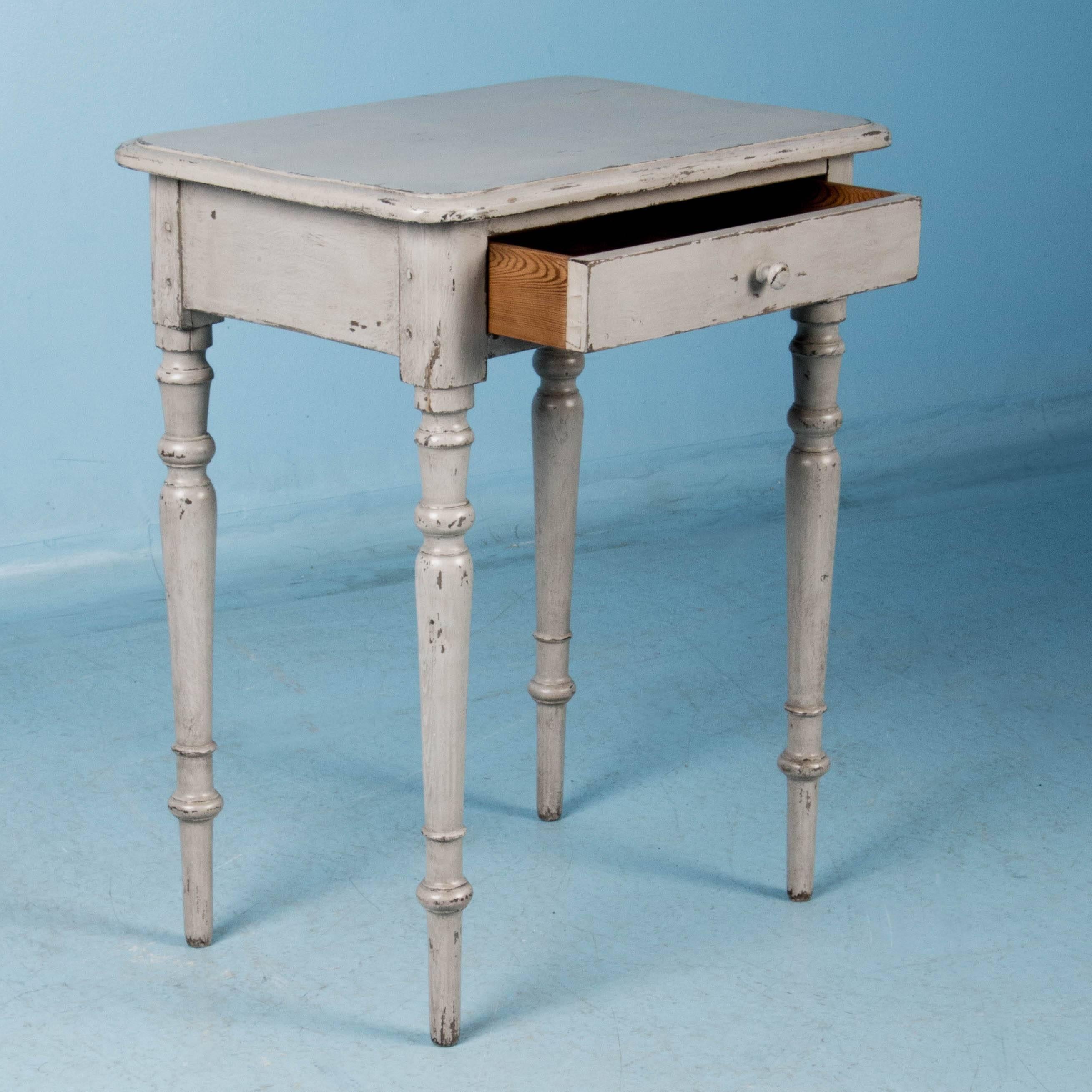 This vintage side table from Denmark is simple and charming with it's softly rounded edges and slightly tapered turned legs. There is a gentle appeal in the gray chalk paint that has been lightly scraped exposing the natural pine beneath, giving