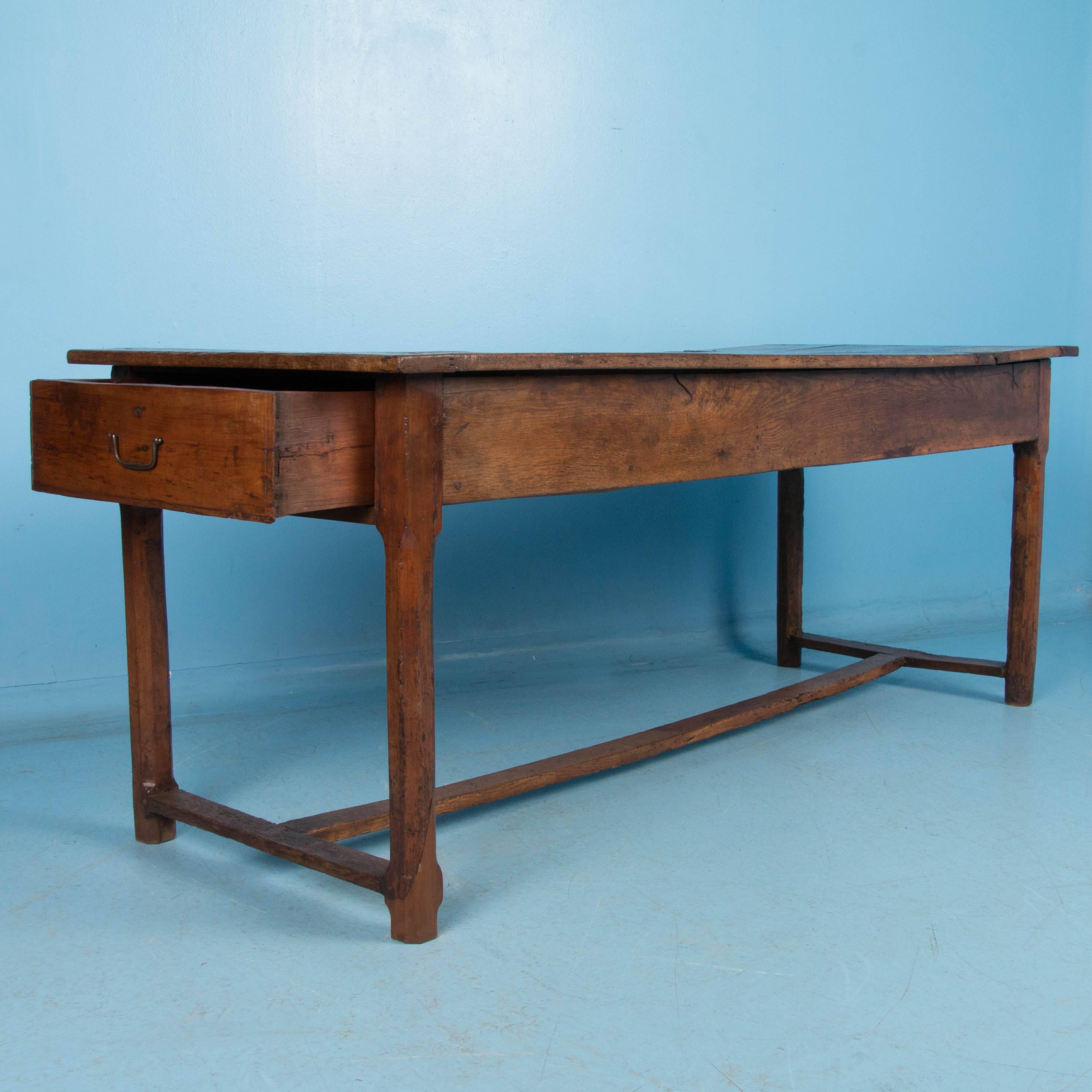 The rich color along with the aged texture of the hardwood, create a remarkable patina that is all original in this farm table. An unusual feature of the table is a hinged section on the top that lifts to expose a large storage space underneath. It