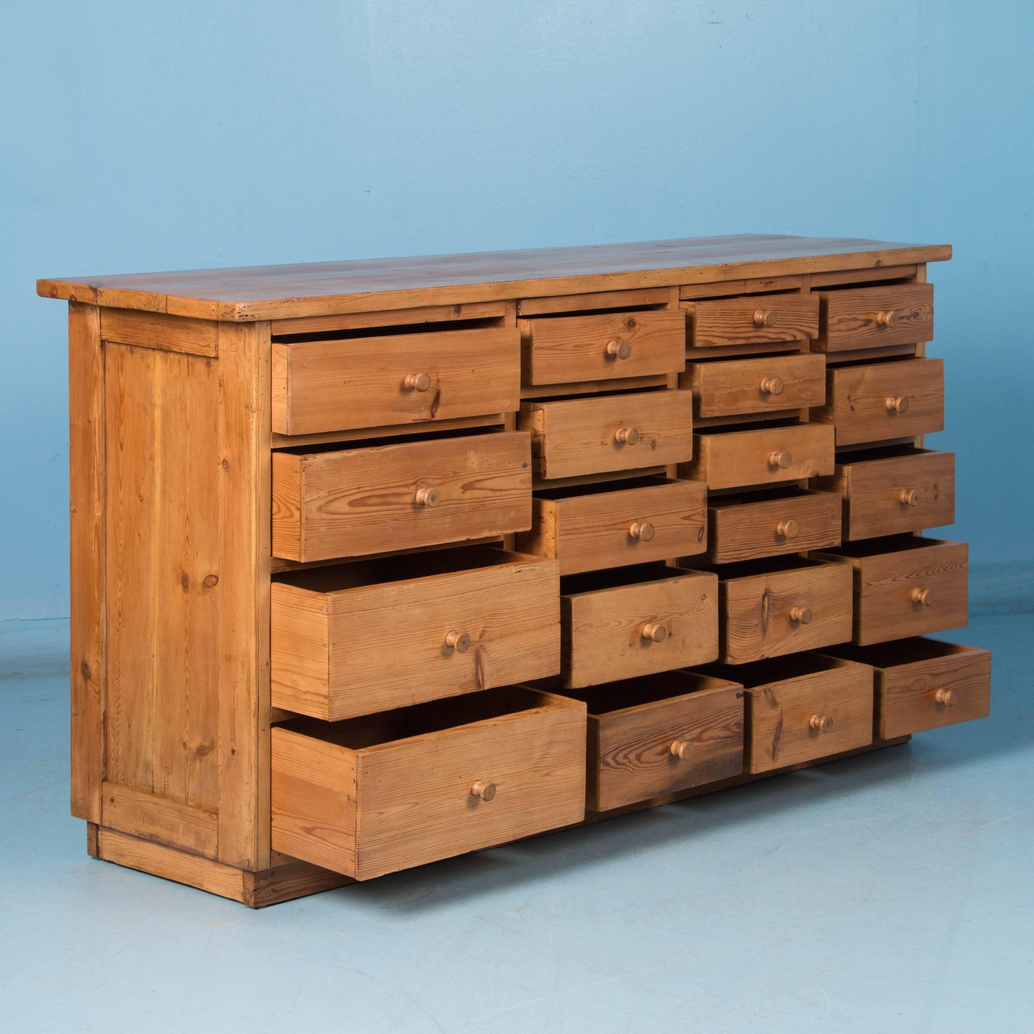 This unique Danish pine sideboard has a country mercantile look with a total of 20 drawers divided into in four columns, each column having a different size drawer which creates great visual appeal along with unique storage options. It is panelled