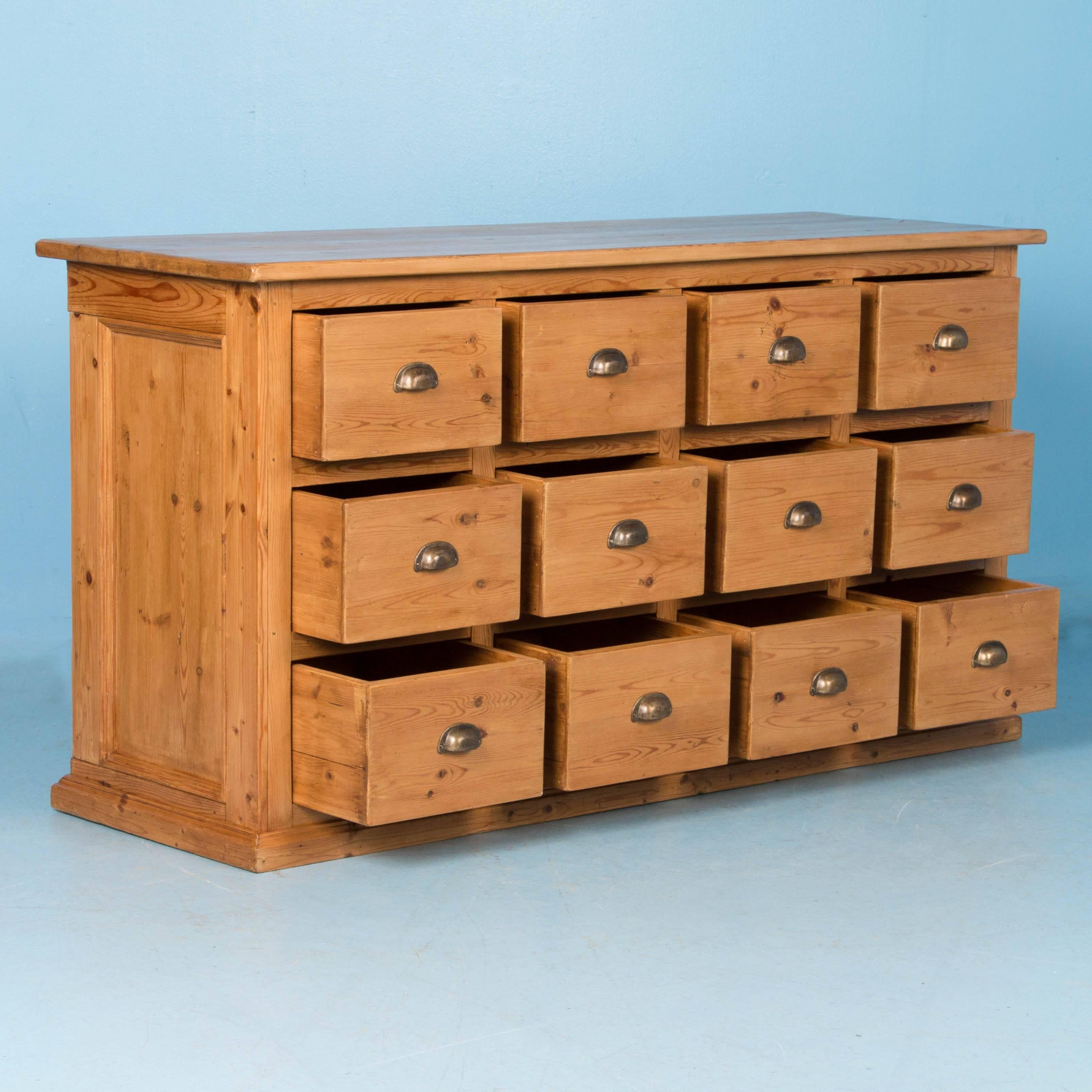 Unique and versatile, this antique pine cabinet was made to be viewed from all sides, with vertical panels on the ends and back. Originally used as a grocer's store counter, the 12 drawers offer ample storage, making for the perfect kitchen island