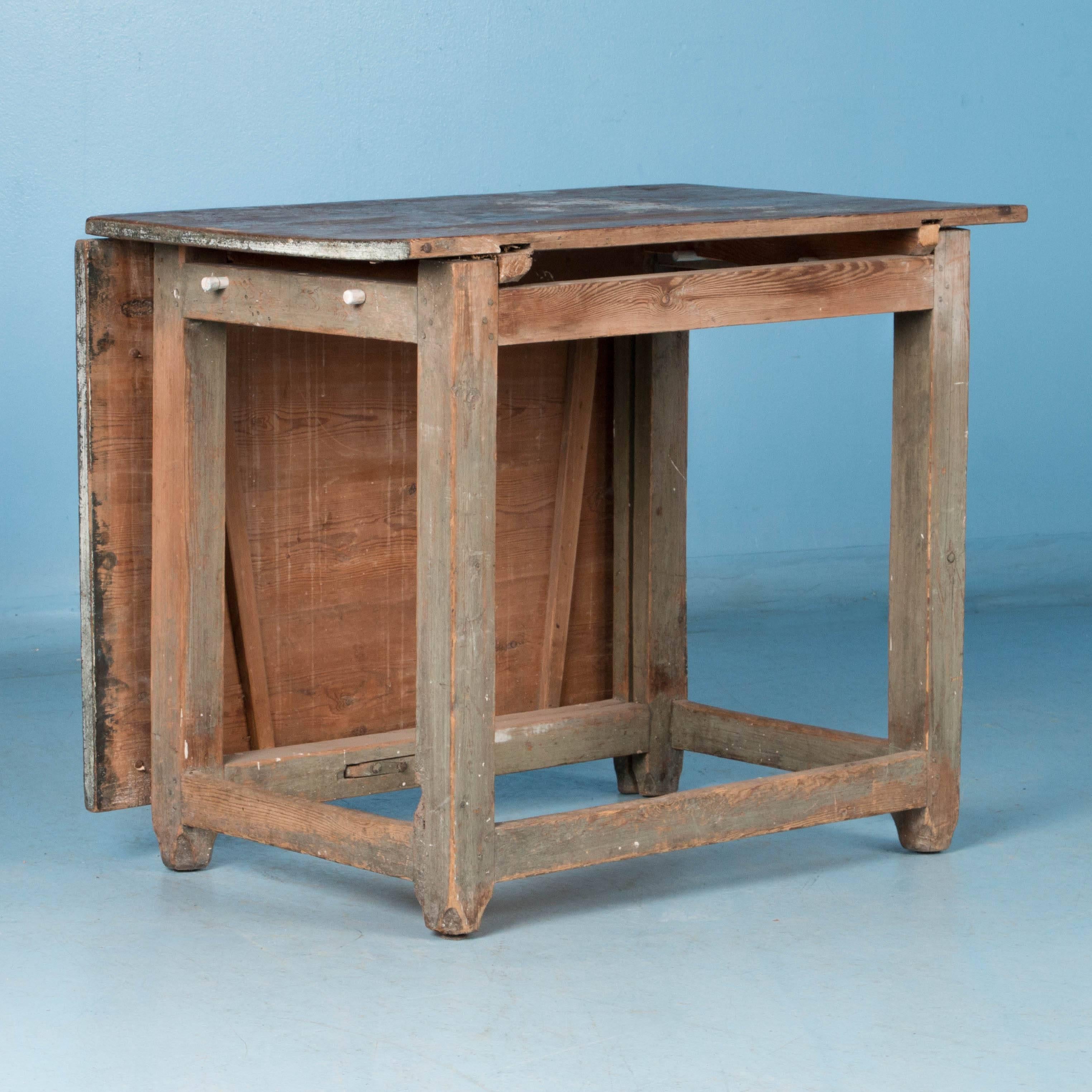 There is wonderful charisma to this sweet drop-leaf table due to the varied colors of paint layered on through the years and now softly distressed. While the top has been worn down to the natural pine, in the large single drop leaf you will see