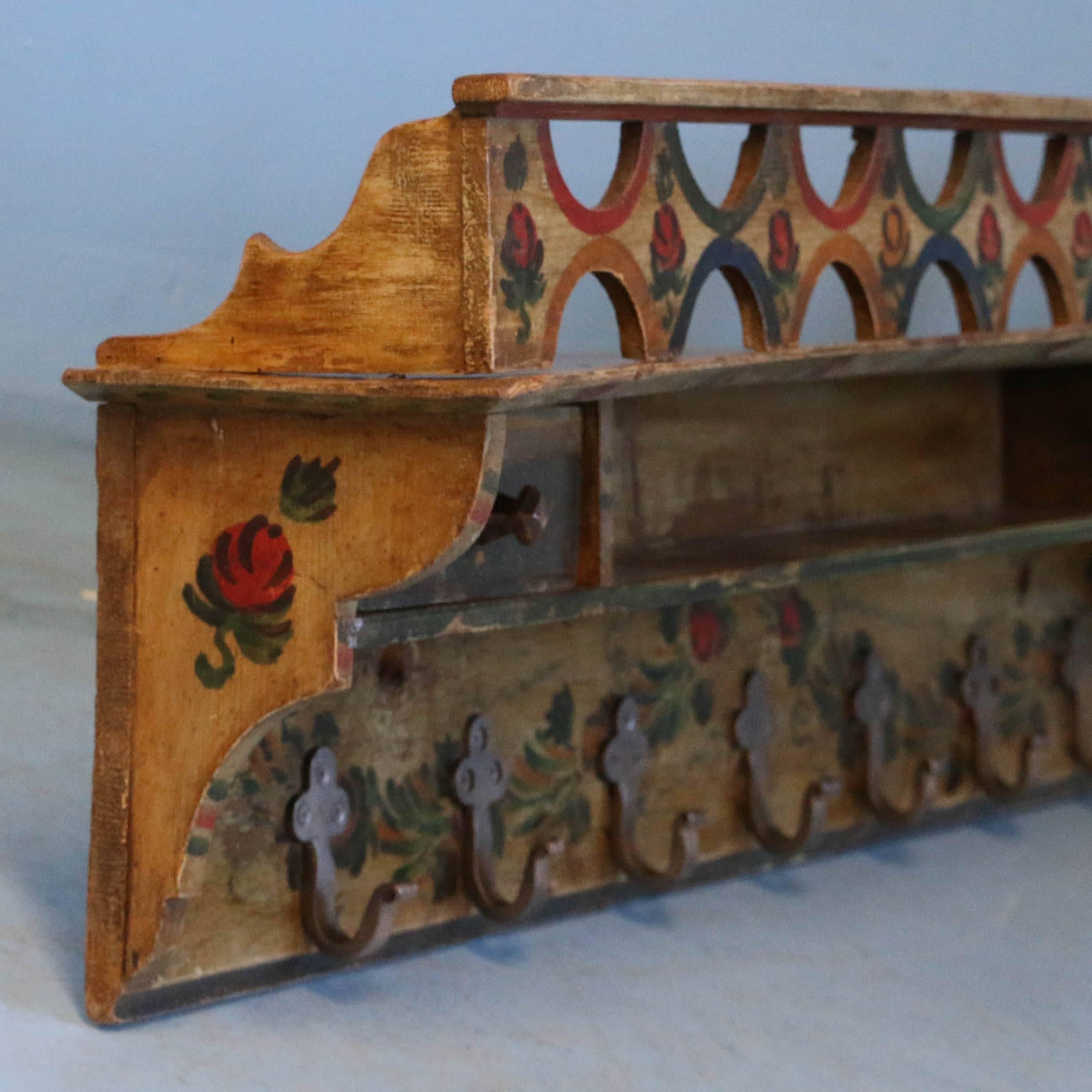 This colors and patina of this wonderful folk art painted wall rack sets this apart from the others. Decorated with a floral design in red, yellow and green over an aged yellow background, it features two small drawers with a shallow shelf between