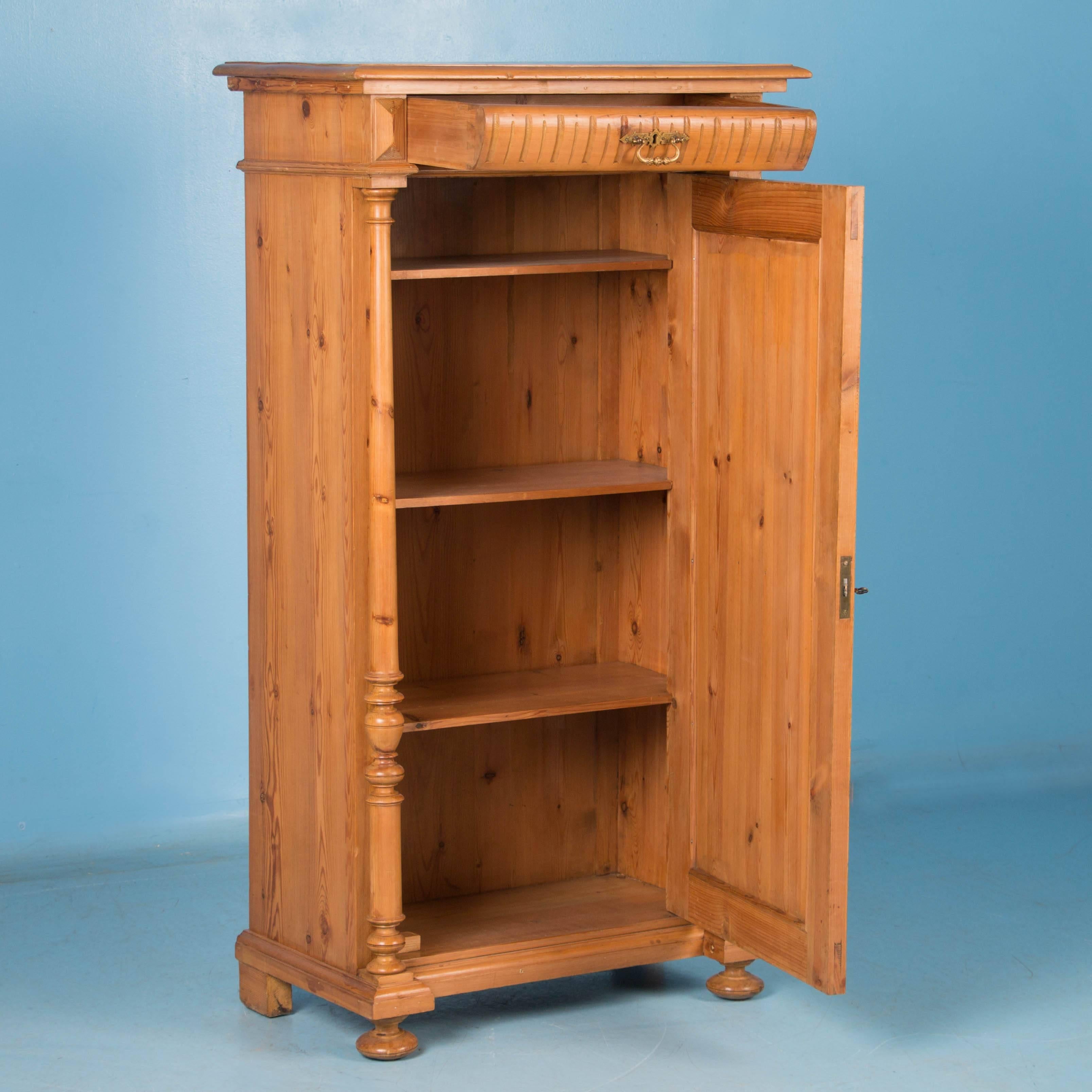  This pine armoire from Denmark radiates European country charm with it's turned column details and intricate carving in the panel door. The abbreviated height and narrow width offer versatility. It has been given a wax finish, bringing out the