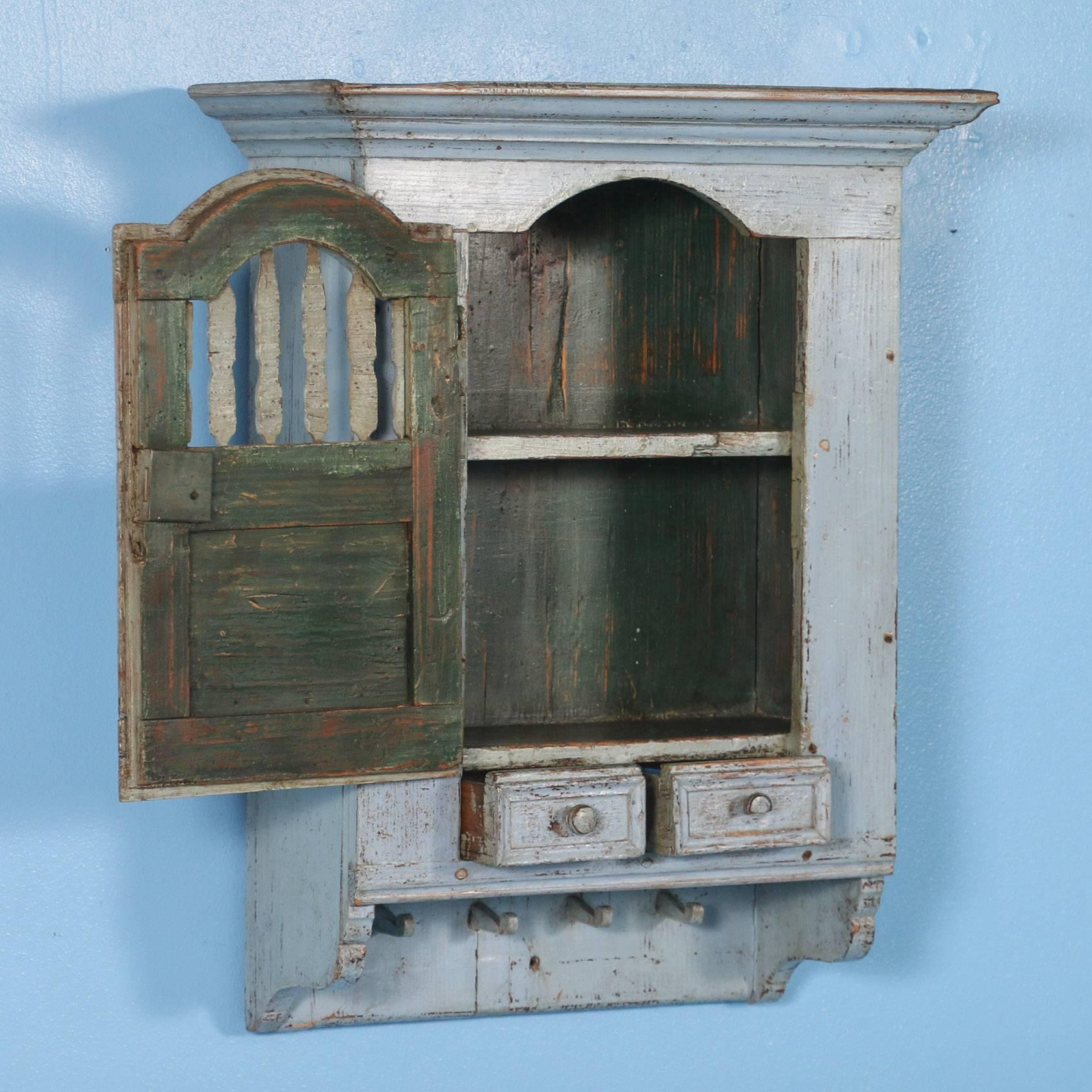 Small blue antique Swedish wall cabinet with original paint.  There is a single door over 2 small drawers with 4 hand carved hanging pegs . This piece has a soft waxed finish with a beautiful slightly worn patina. This would be a great addition to a