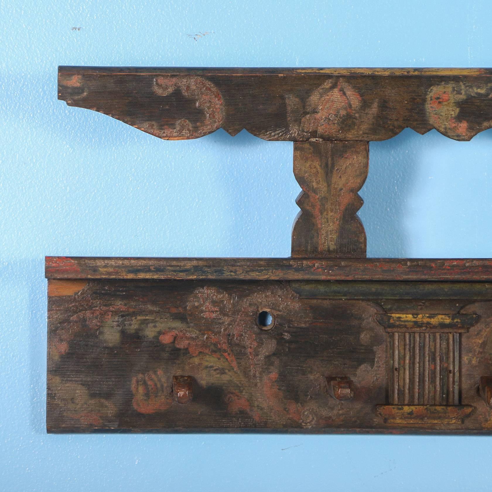Antique Hungarian wall rack with original painted and carved details. The dark green hues almost look black, while the aged red flowers and flourishes were traditional folk art designs of the period. The 10 wood pegs were hand carved and are ready
