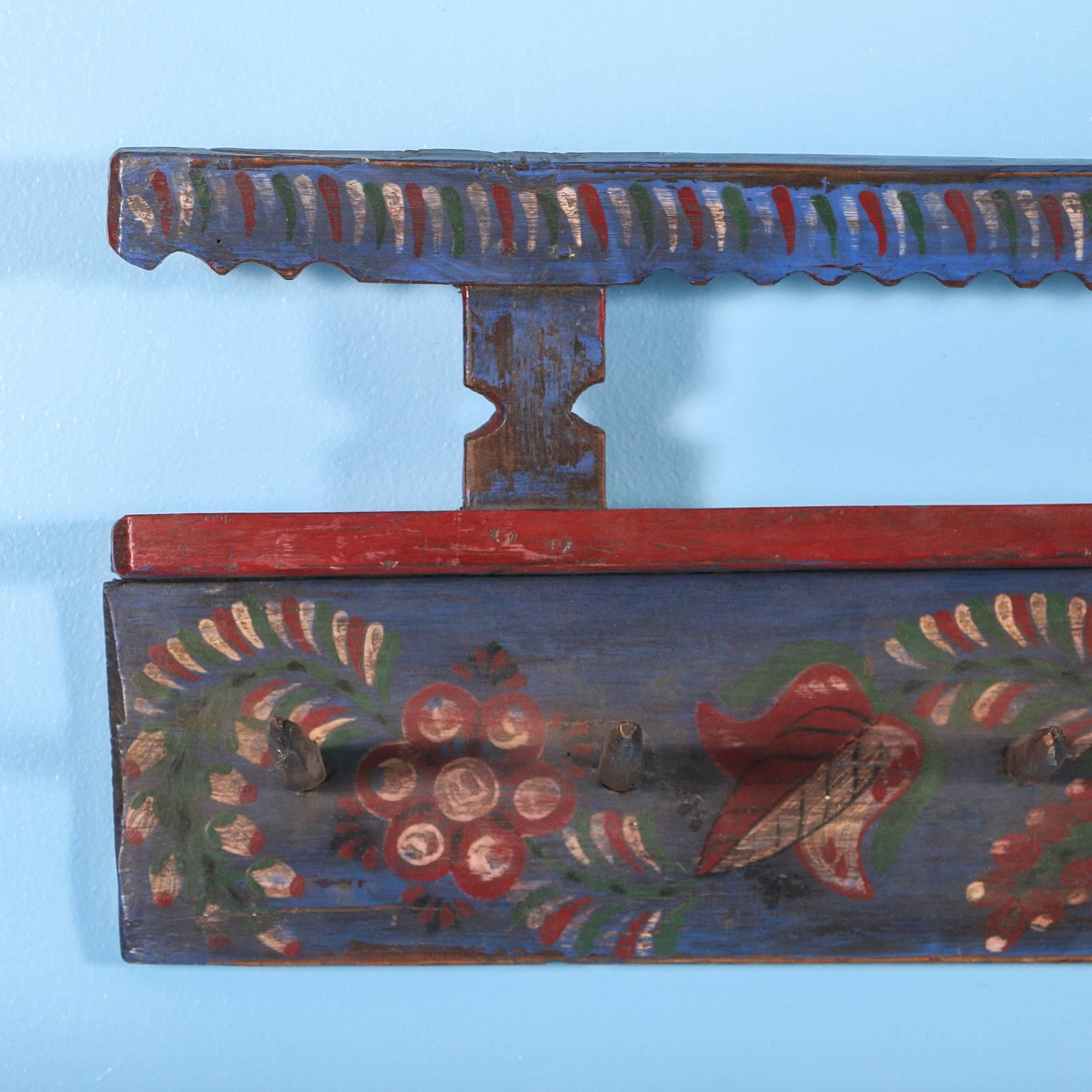 This charming antique hanging wall rack is just over 8' long and still maintains its original blue paint with traditional folk art flowers and vines in red, green and white. The 15 wooden pegs were hand carved and painted blue as well. This rack was